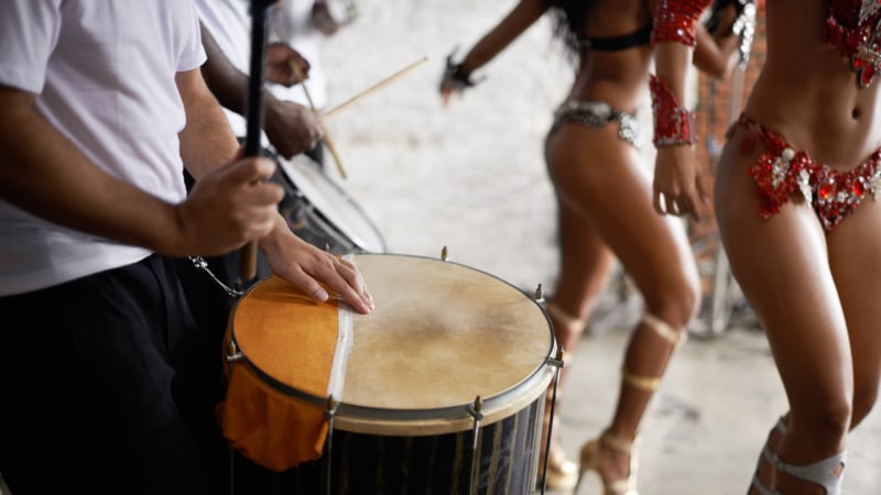 Ein professioneller Schlagzeuger spielt in einer Musikgruppe mit brasilianischen Tänzern bei einer Live-Performance in Kostümen