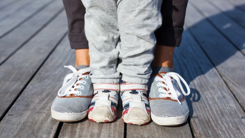 Kinder- und Erwachsenenbeine und -füße in Sneakers nebeneinander auf einem Holzuntergrund