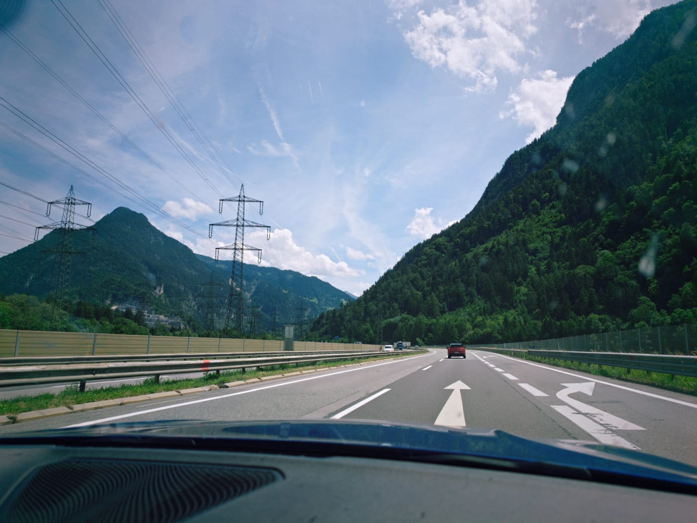 View through a car windshield of an Austrian highway running between green mountains and power lines
