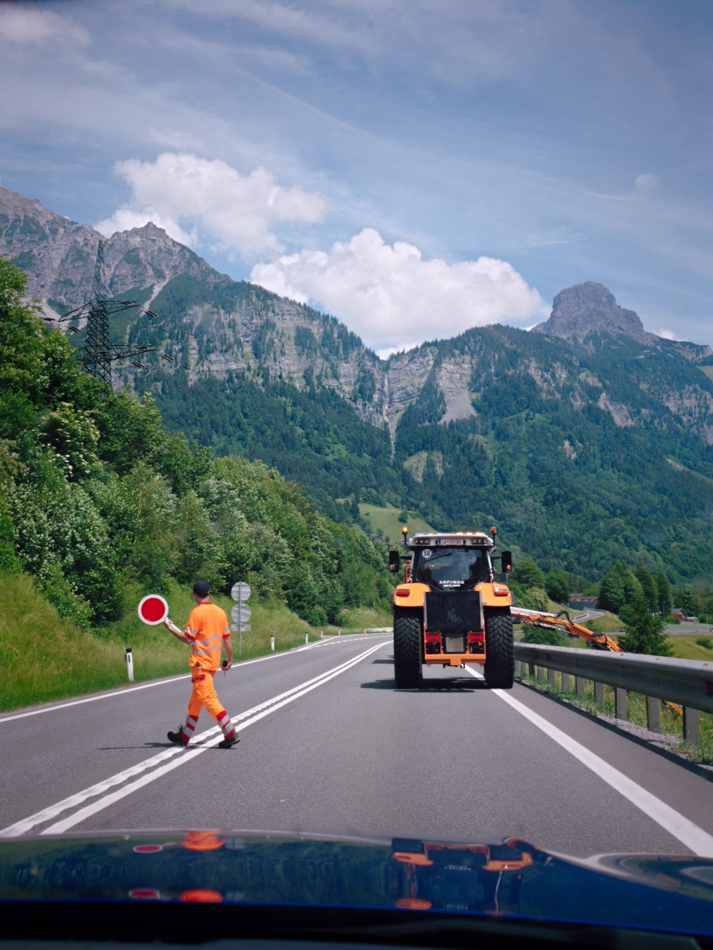 Road worker stopping traffic beside a maintenance vehicle on a mountain road in the Austrian Alps