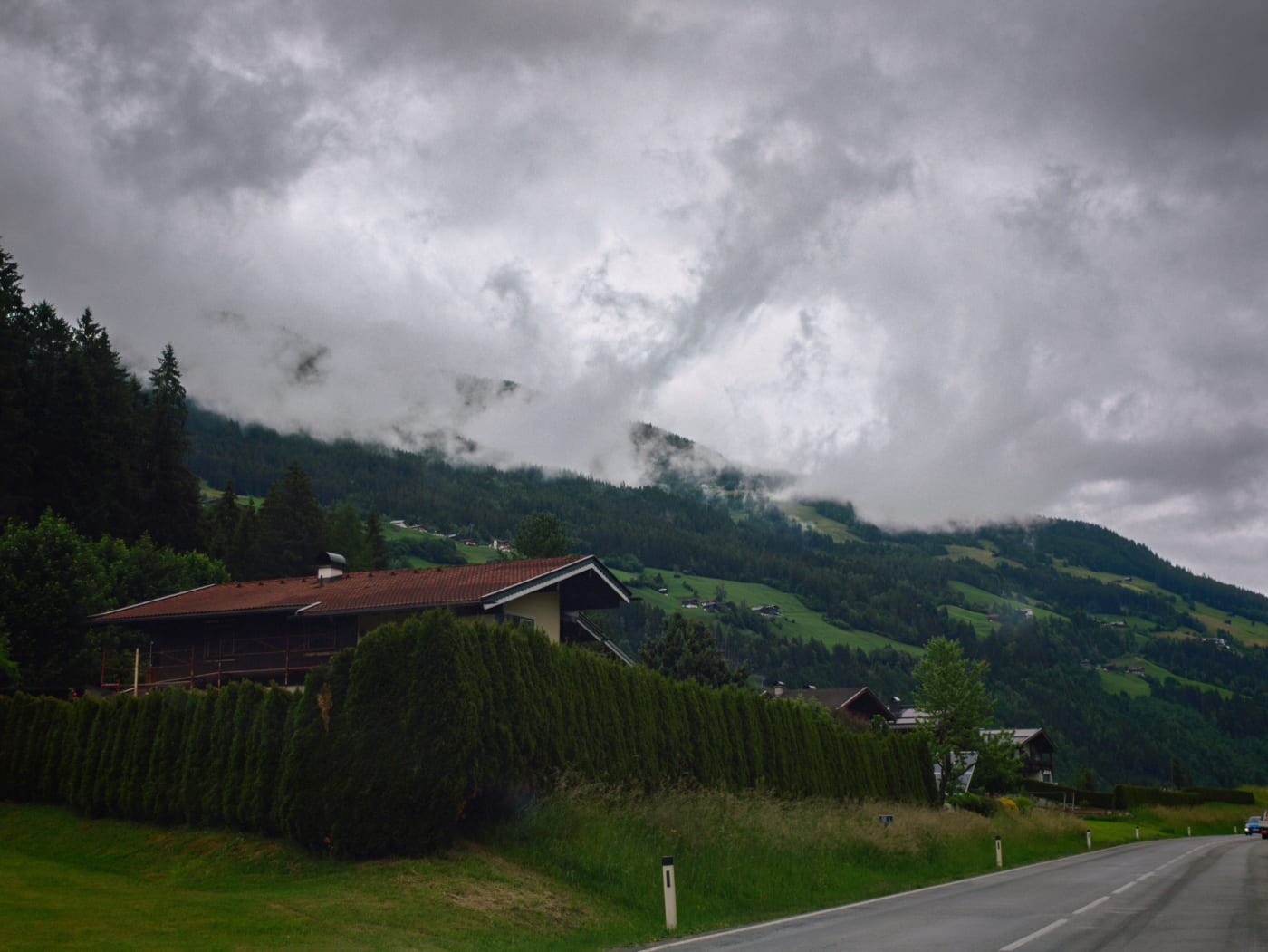 Alpine road curving past chalets and green hills under heavy low clouds