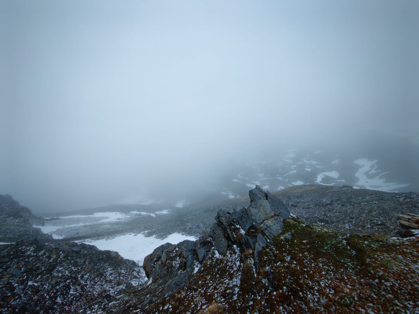 Foggy high alpine ridge with patches of snow and dark rocks fading into cloud