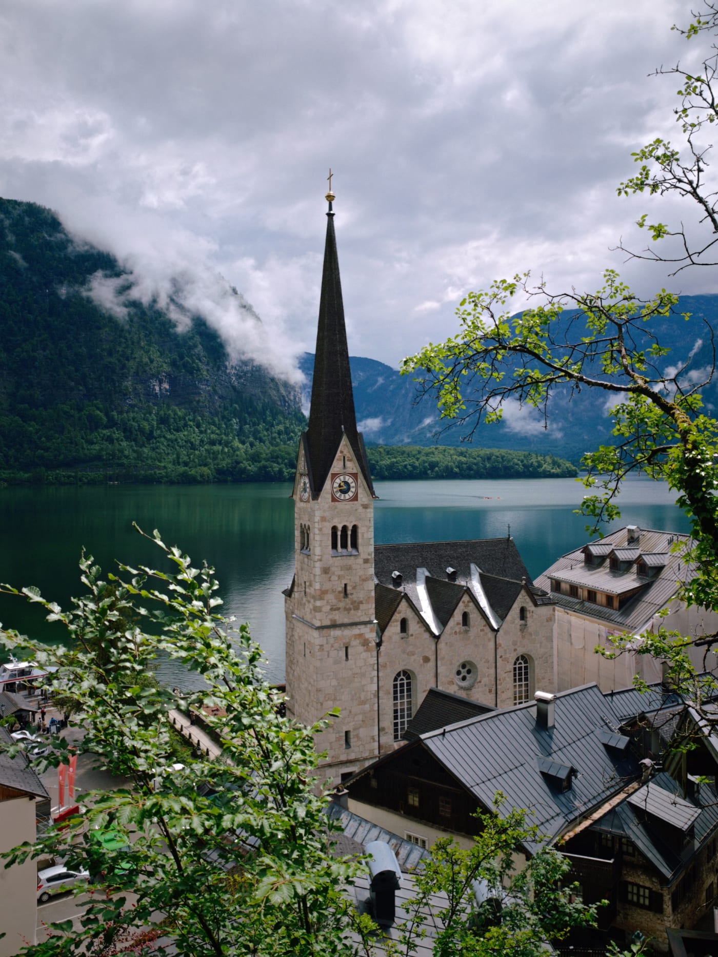 Church steeple above Hallstatt rooftops with the lake and misty mountains behind it