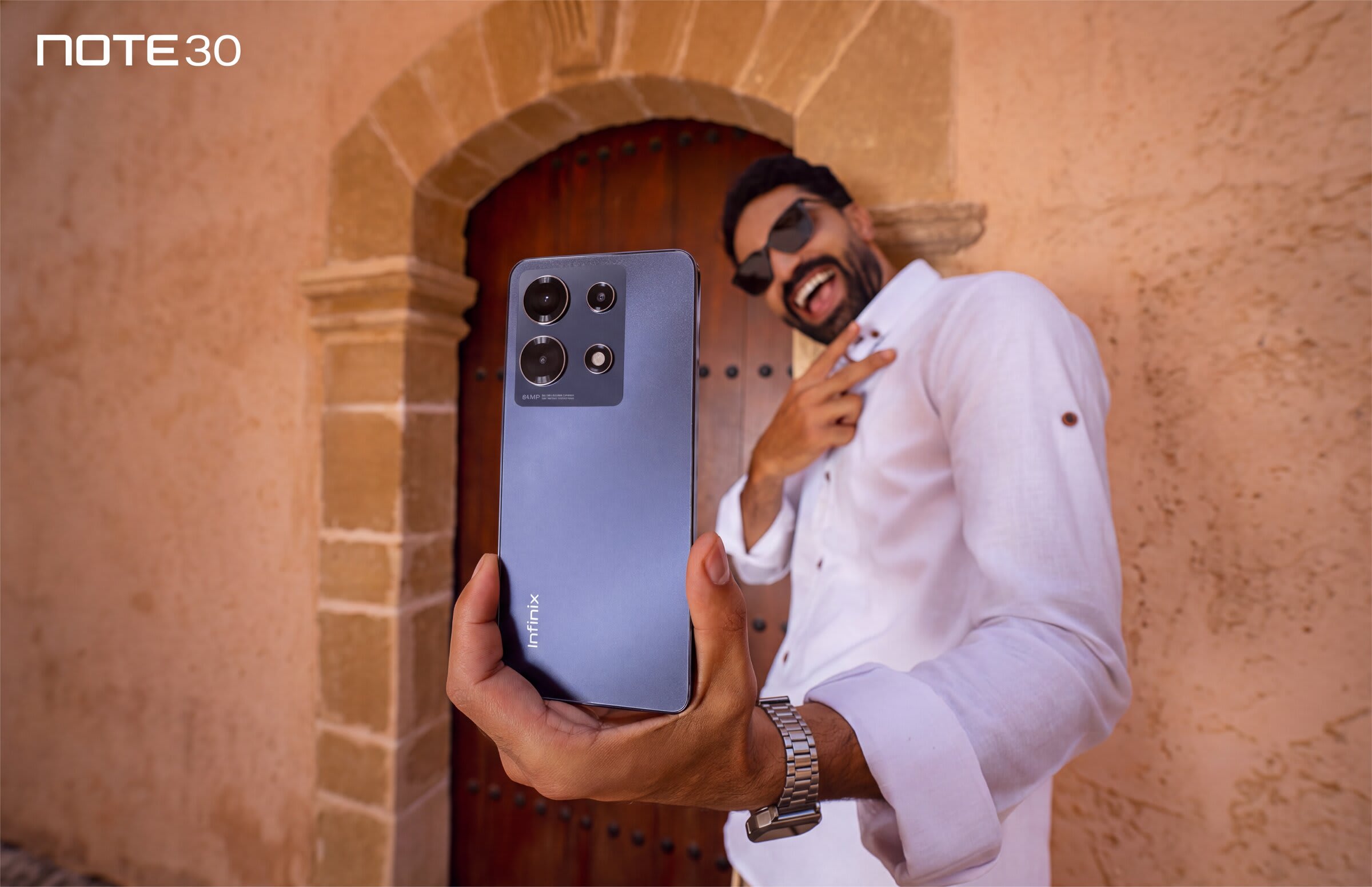 Infinix Note 30 — homme souriant tenant le smartphone devant une porte traditionnelle marocaine