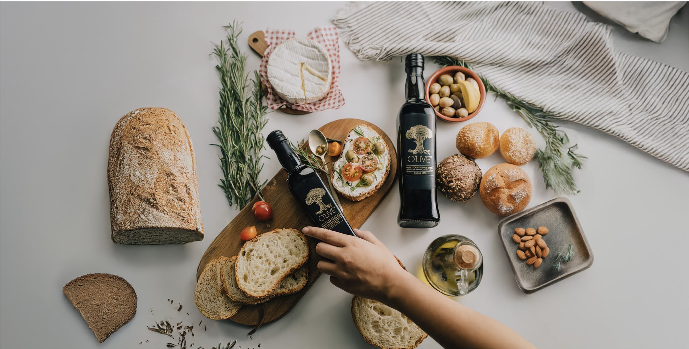 O'live — bouteilles d'huile d'olive, pains et fromage sur une table claire