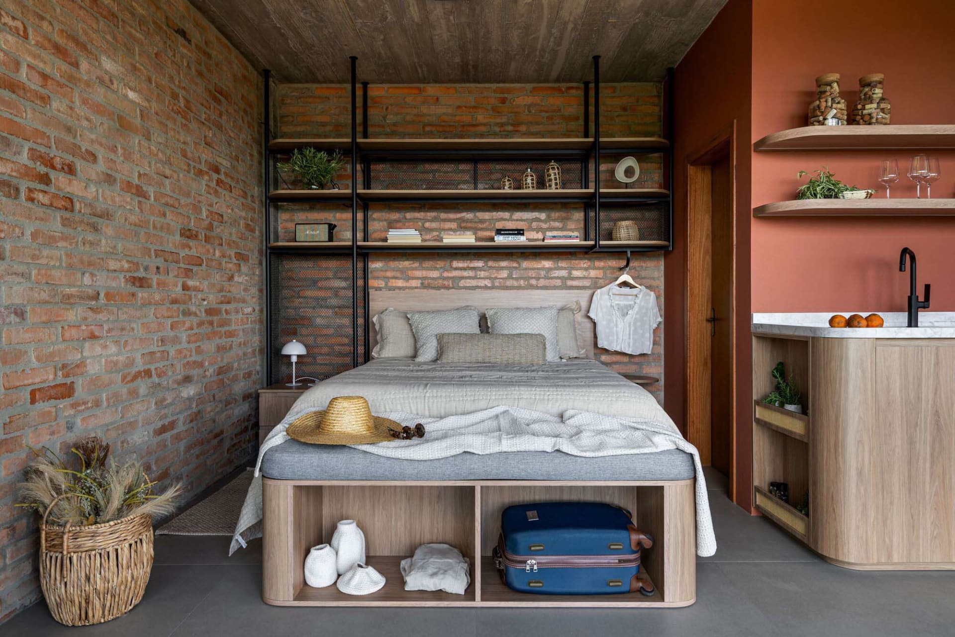 A modern industrial bedroom with a wooden bed and shelving unit containing decorative items.