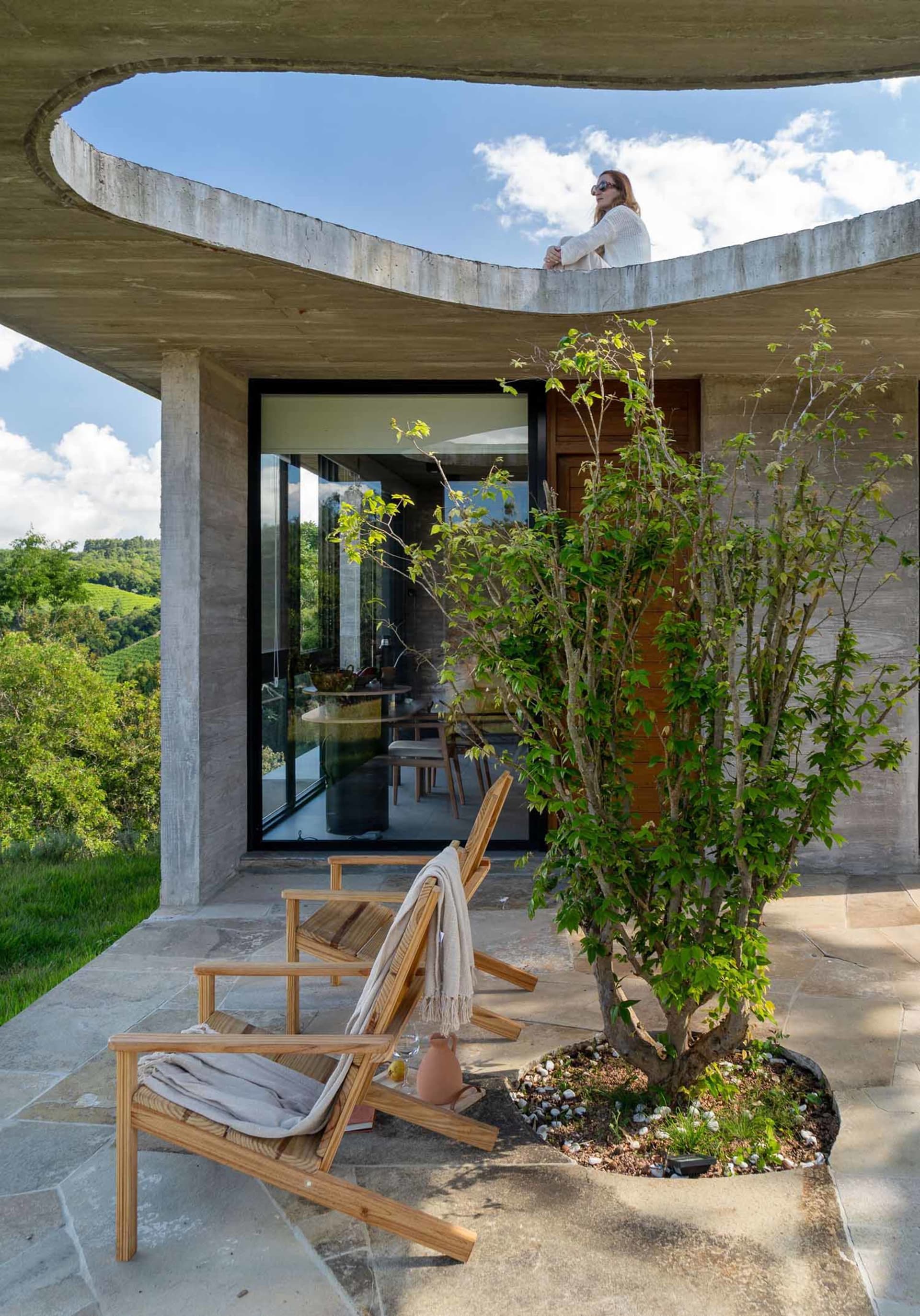 A modern residential home with a concrete exterior, featuring a balcony overlooking green hills.