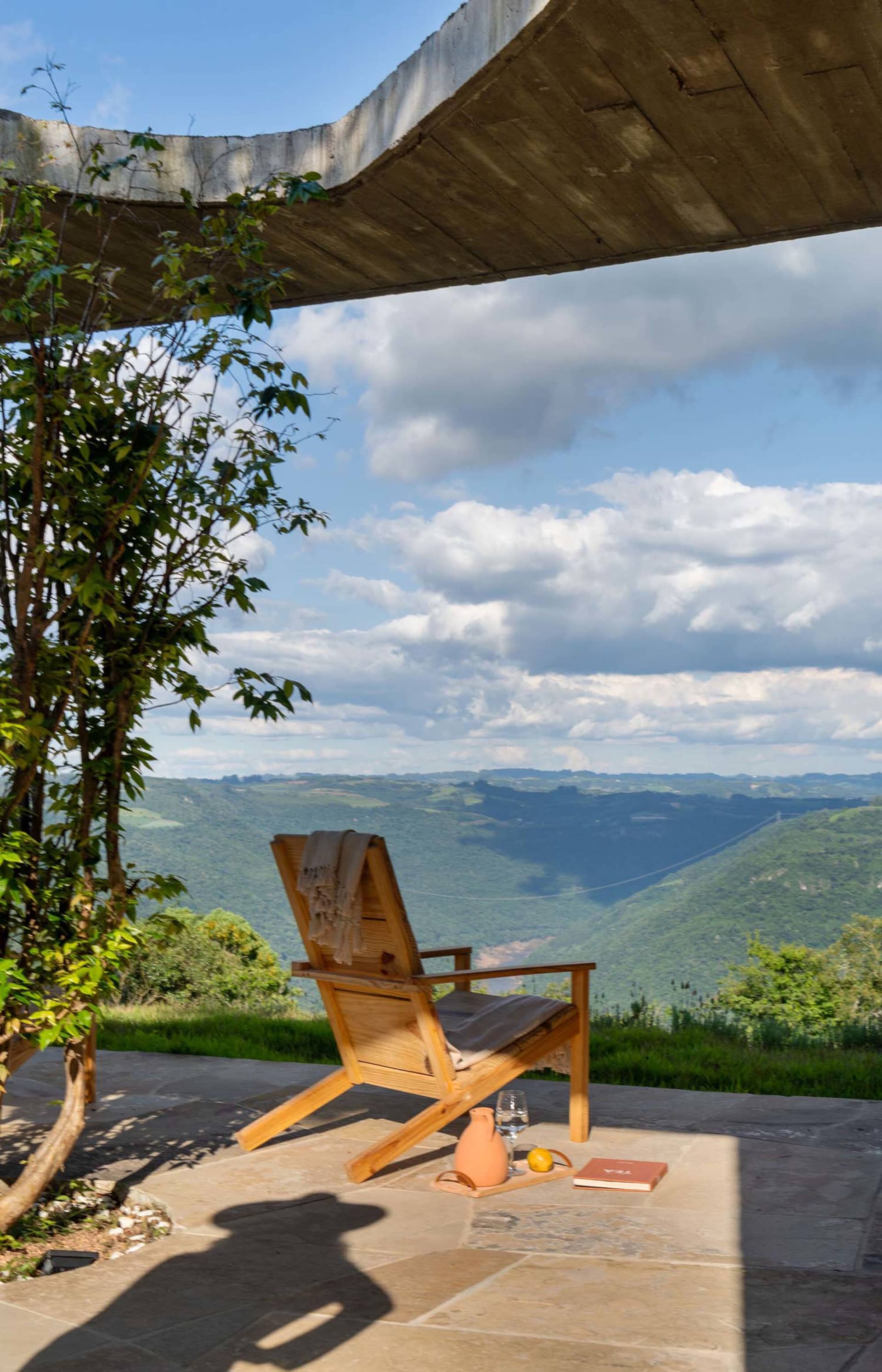 A modern wooden viewing chair placed on a stone veranda overlooking a scenic landscape.