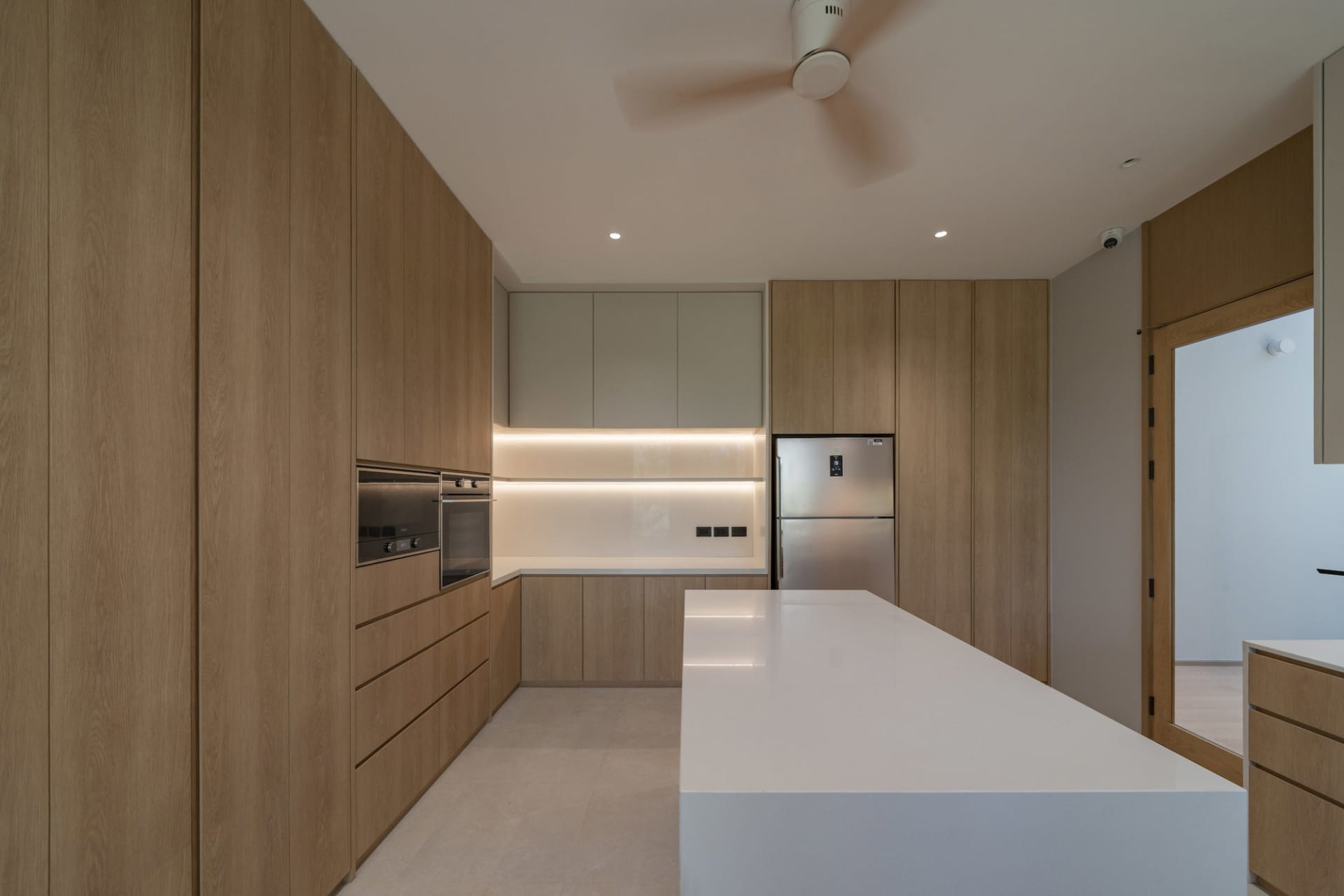 Modern minimalist kitchen featuring wooden cabinets, white countertops, and integrated appliances.