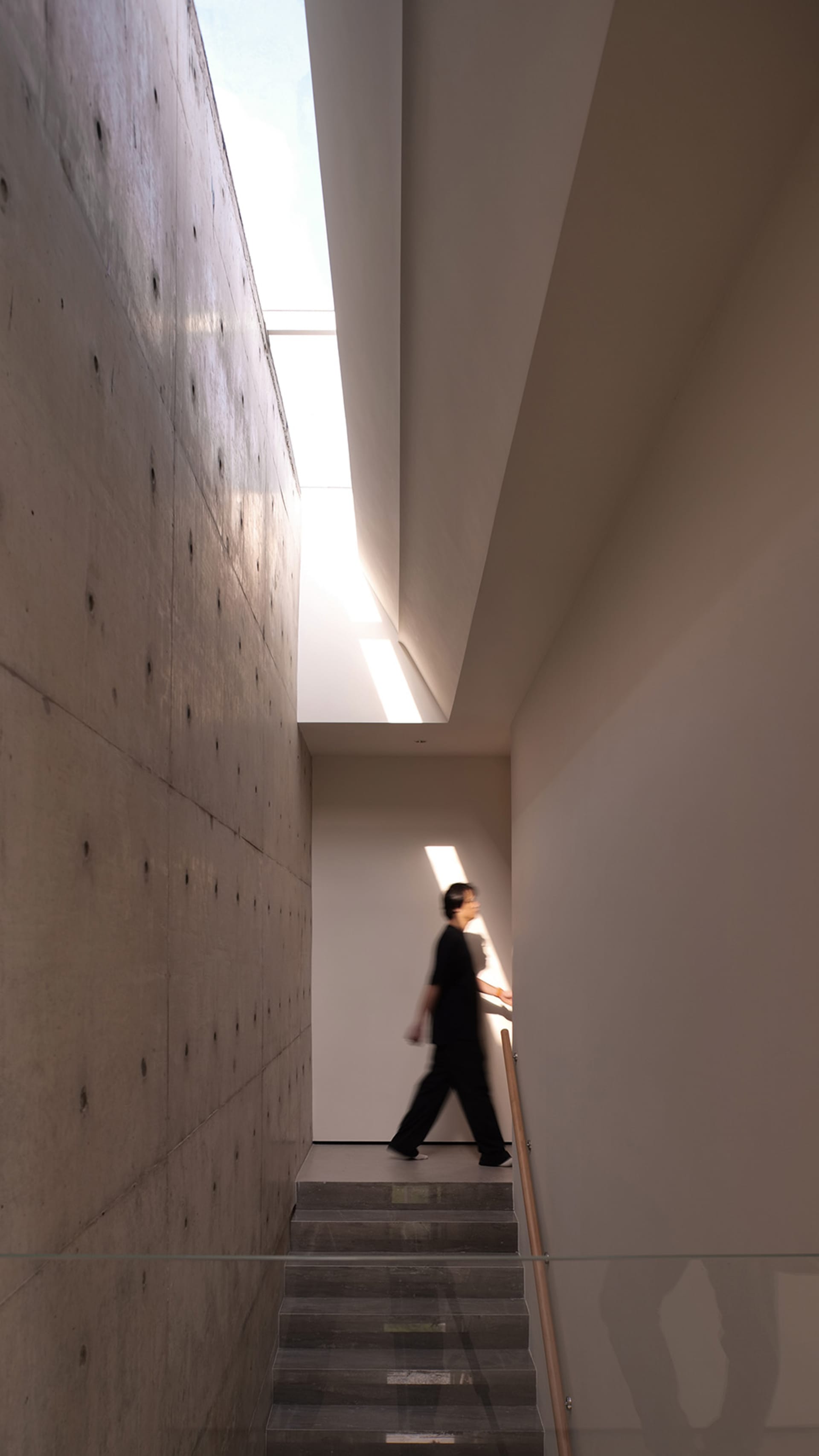 A modern, industrial-style staircase with a concrete wall and glass railing.