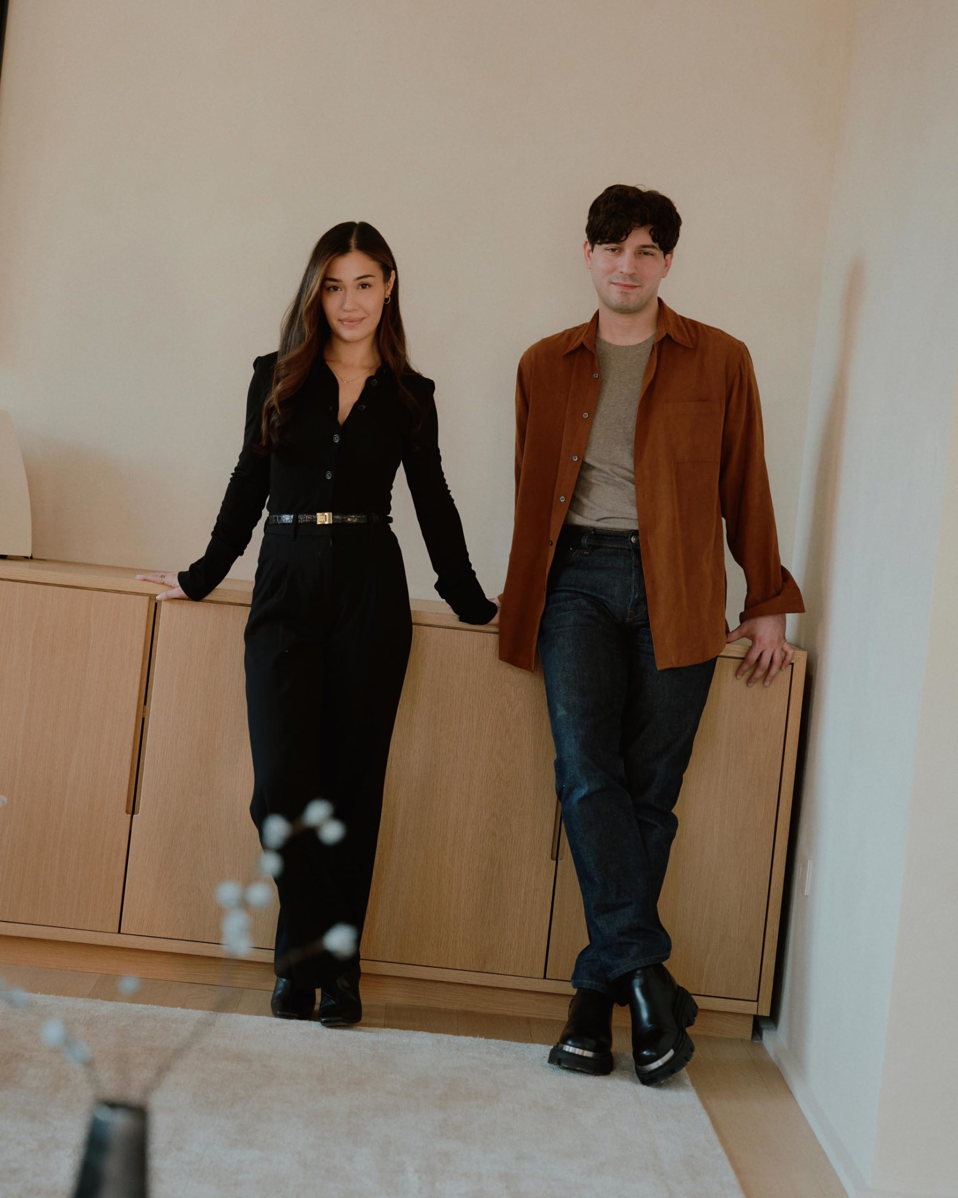A man and a woman wearing stylish clothing standing next to each other in a modern interior setting.