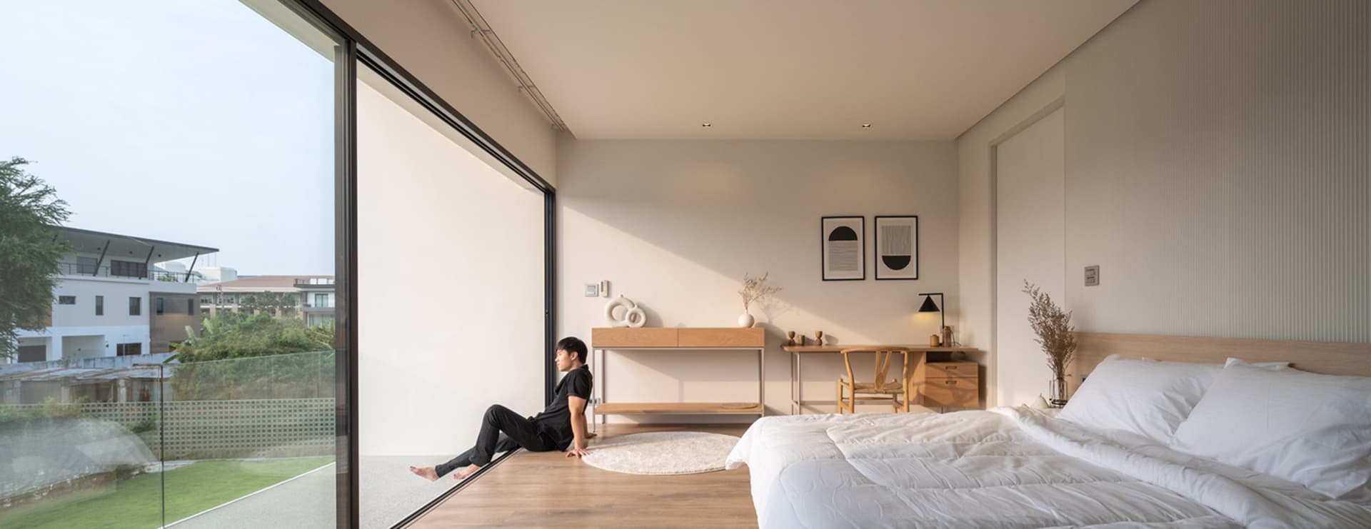 Modern minimalist bedroom with glass wall, wooden floor, and white furniture.
