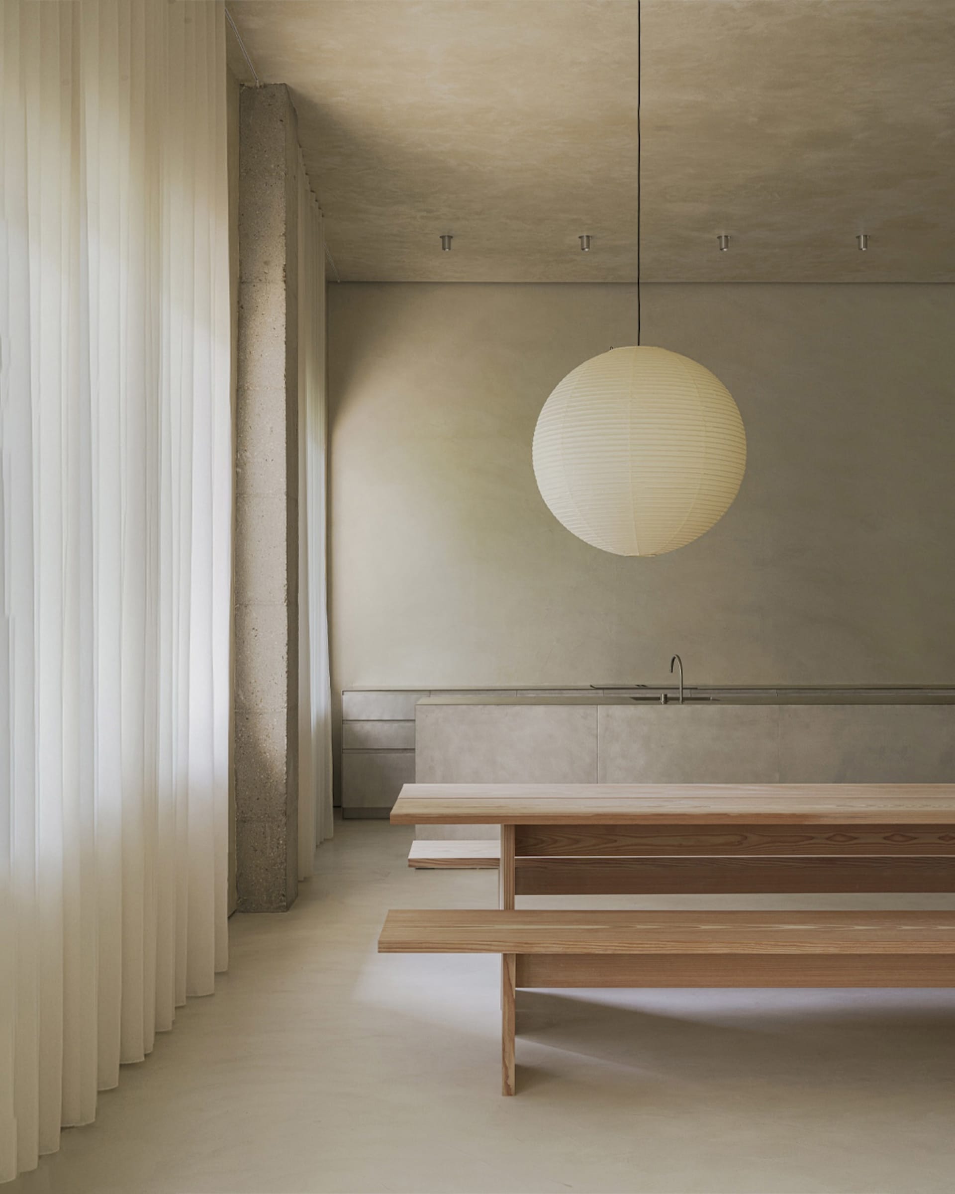 A minimalist interior with concrete walls, a wooden bench, and a paper lantern light fixture.