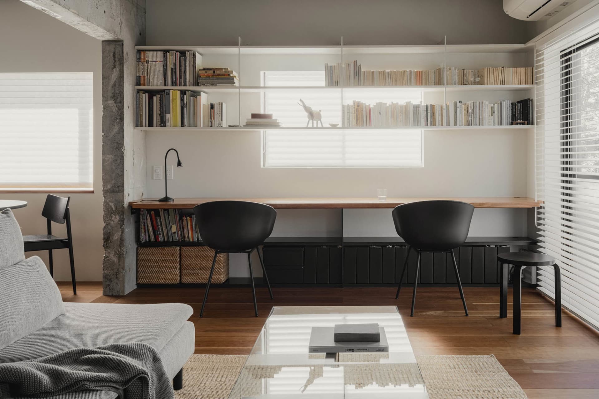 A minimalist living room featuring modern shelves with various books and decorative items, a grey couch, a glass coffee table