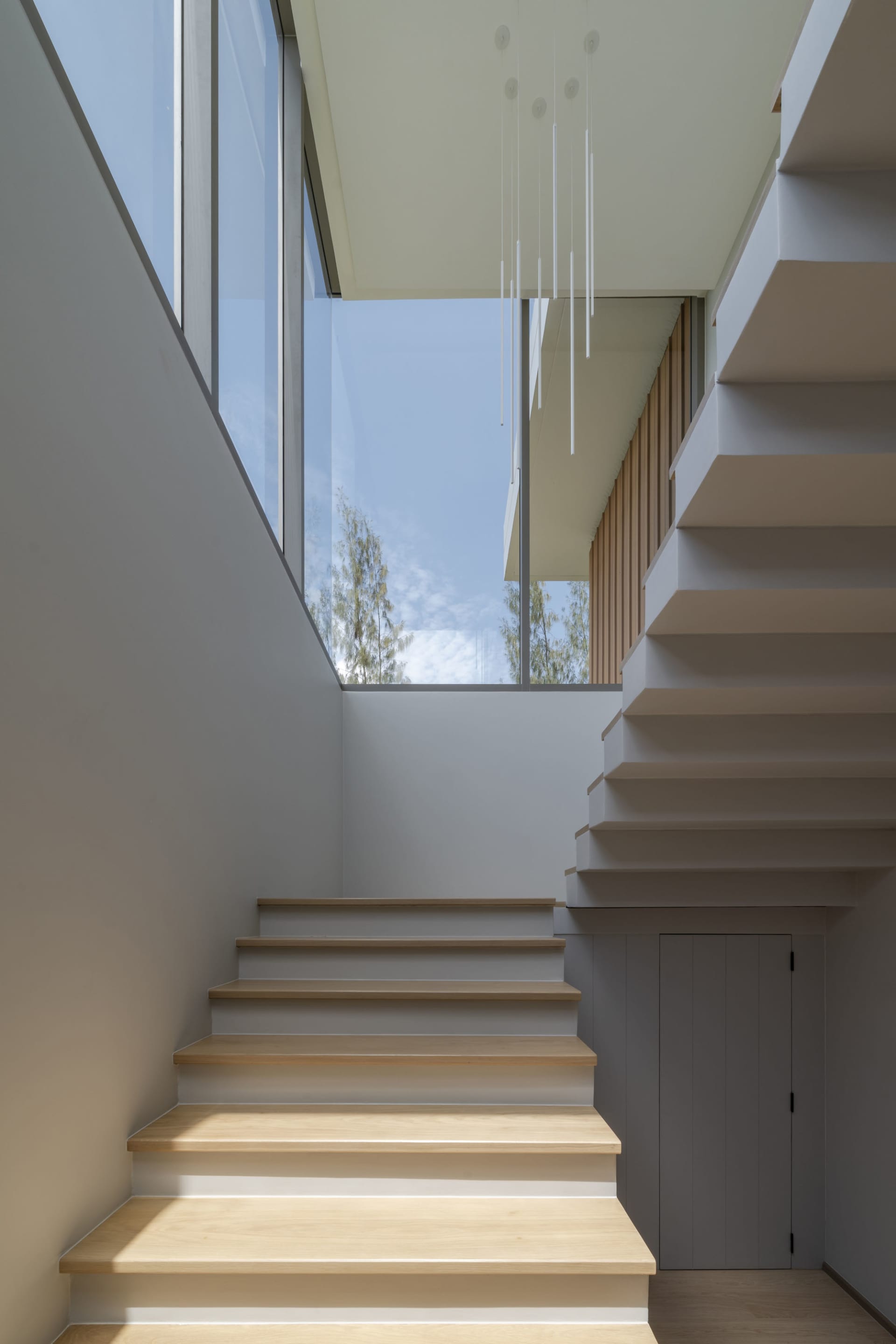 Modern interior space featuring wooden stairs with glass wall and ceiling window.