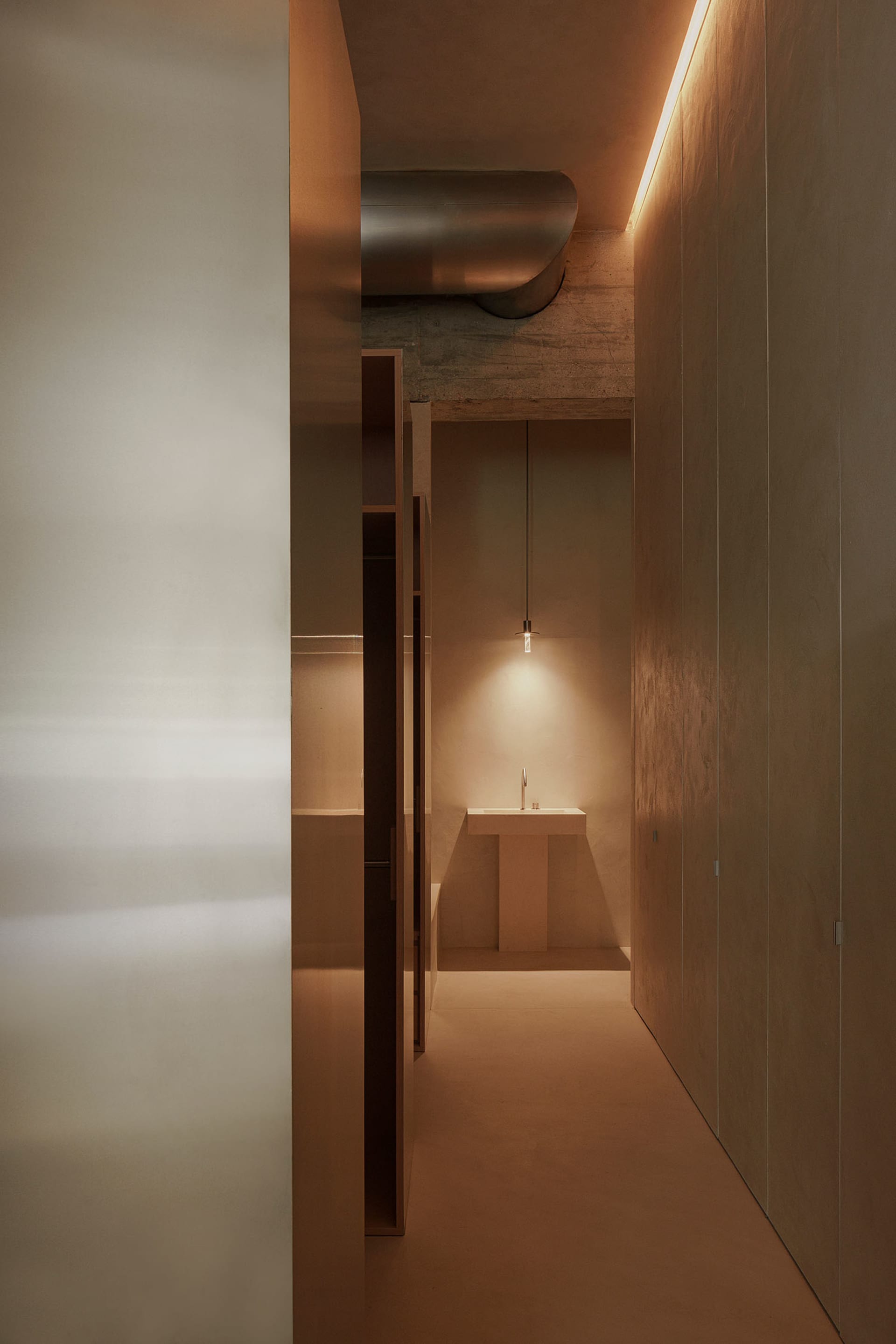 A modern minimalist bathroom with concrete walls and floor, featuring a sleek sink and lighting.