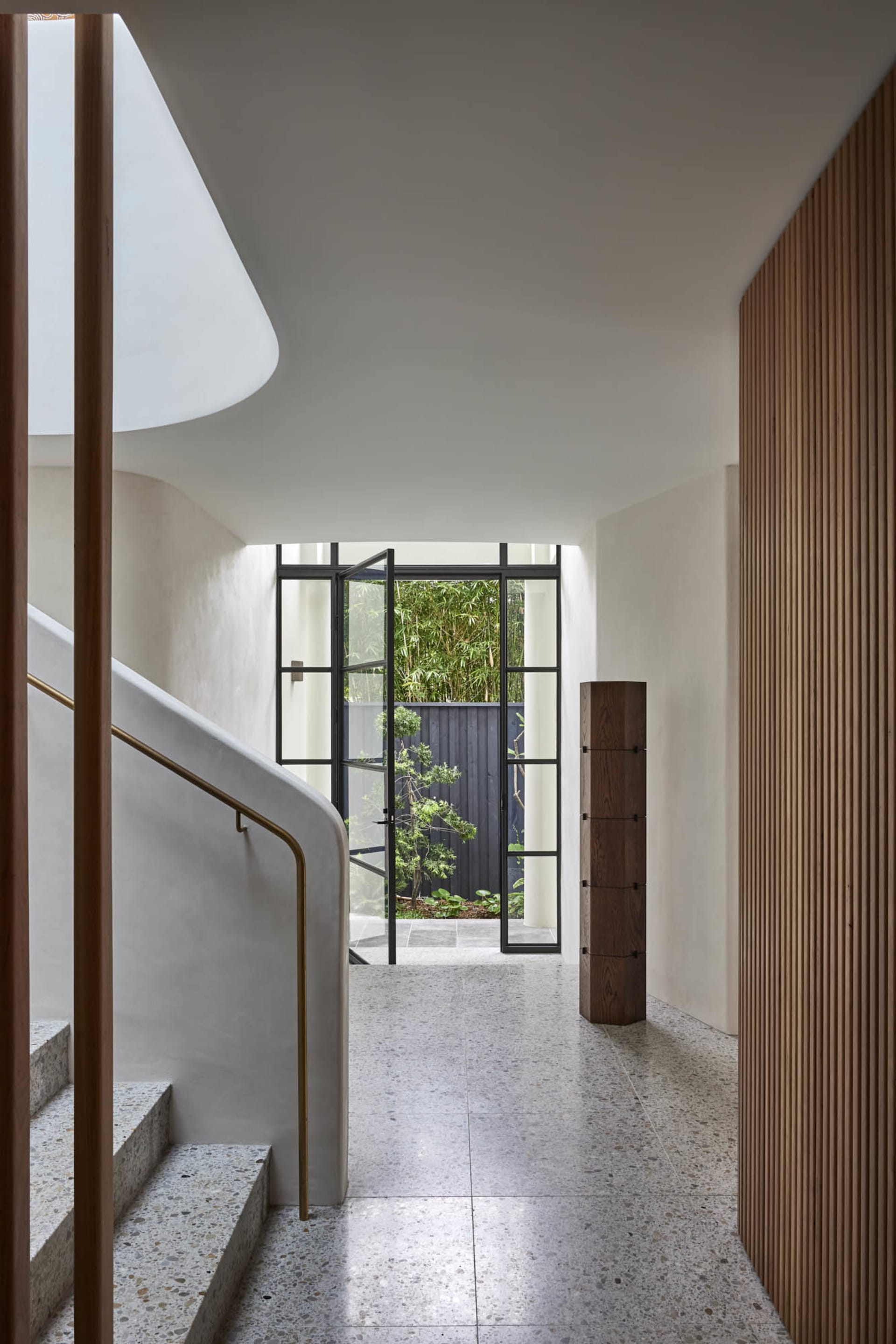 Modern minimalist entrance hall featuring a concrete staircase, glass door, wood accents, and a view of green foliage outside