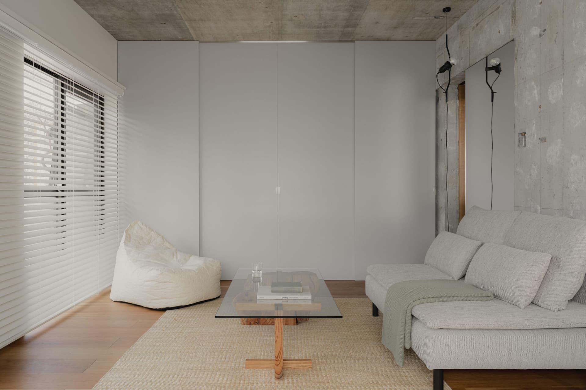 A modern minimalist living room with concrete walls, canvas furniture, and a glass coffee table on a wooden floor.