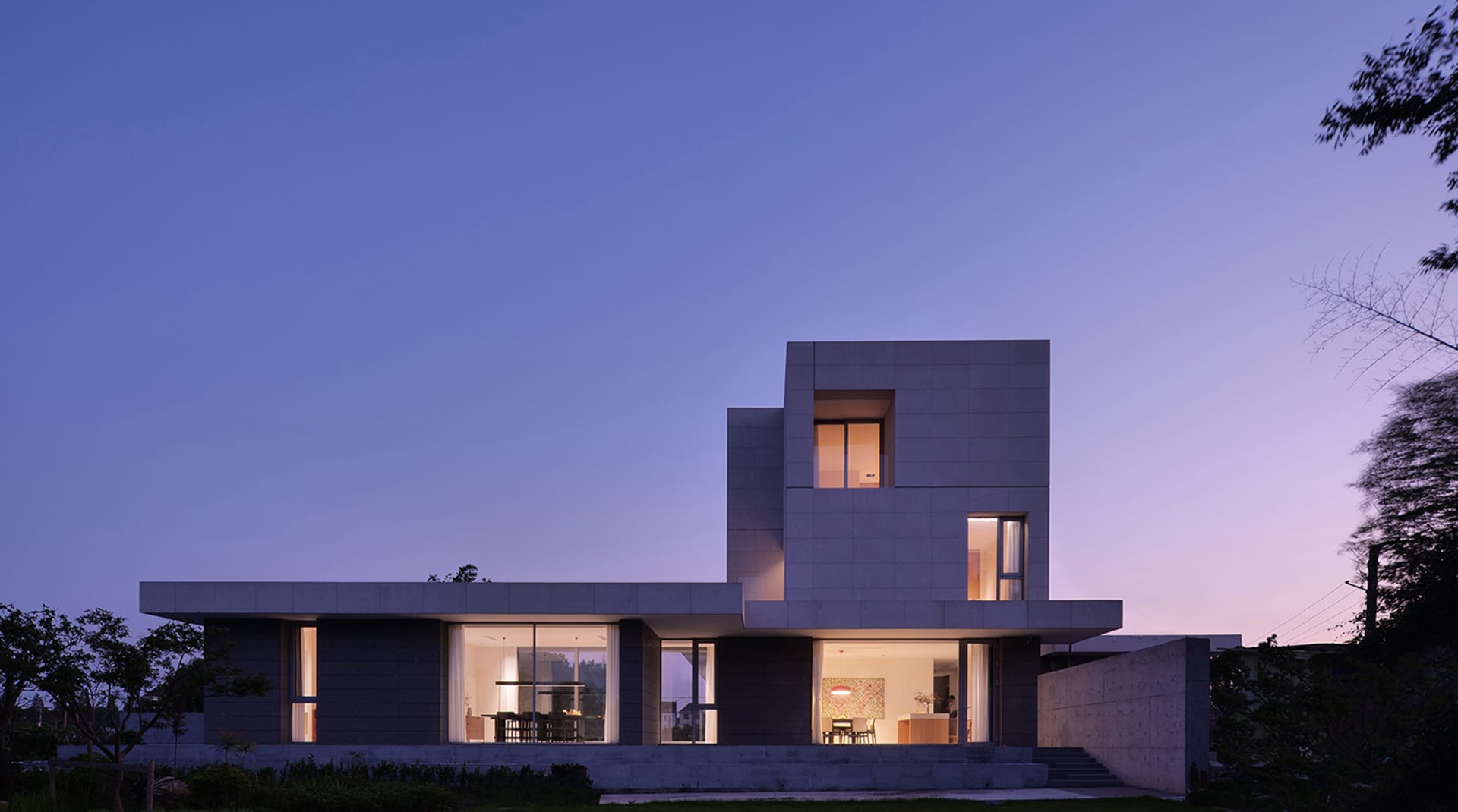 Modern residential house with concrete exterior at dusk with lights on inside