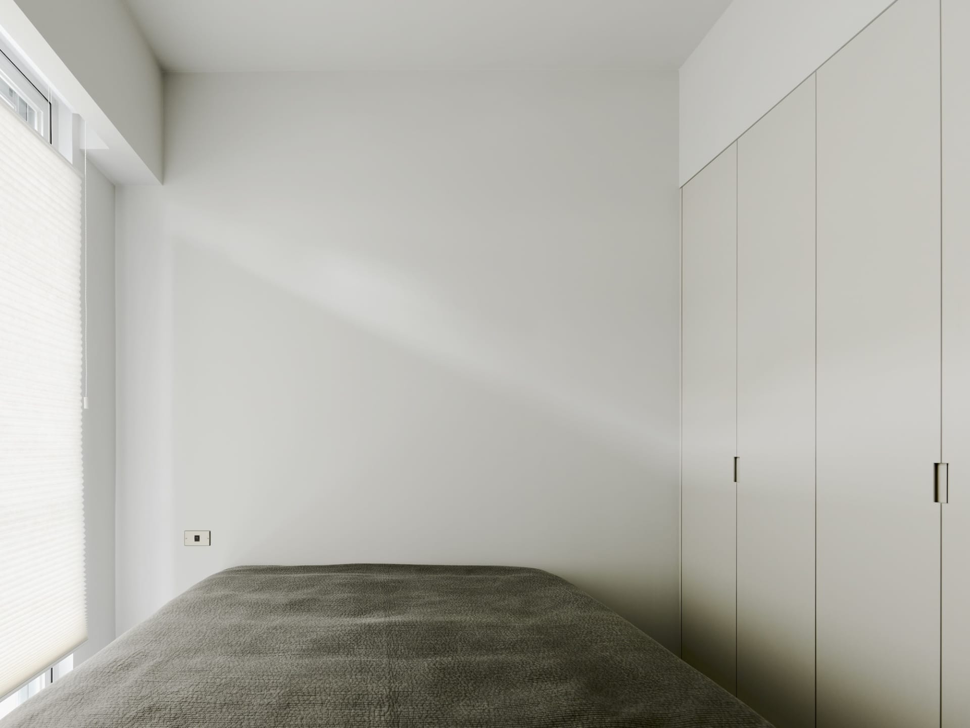 A minimalist bedroom features a soft fabric-covered bed against a white wall.