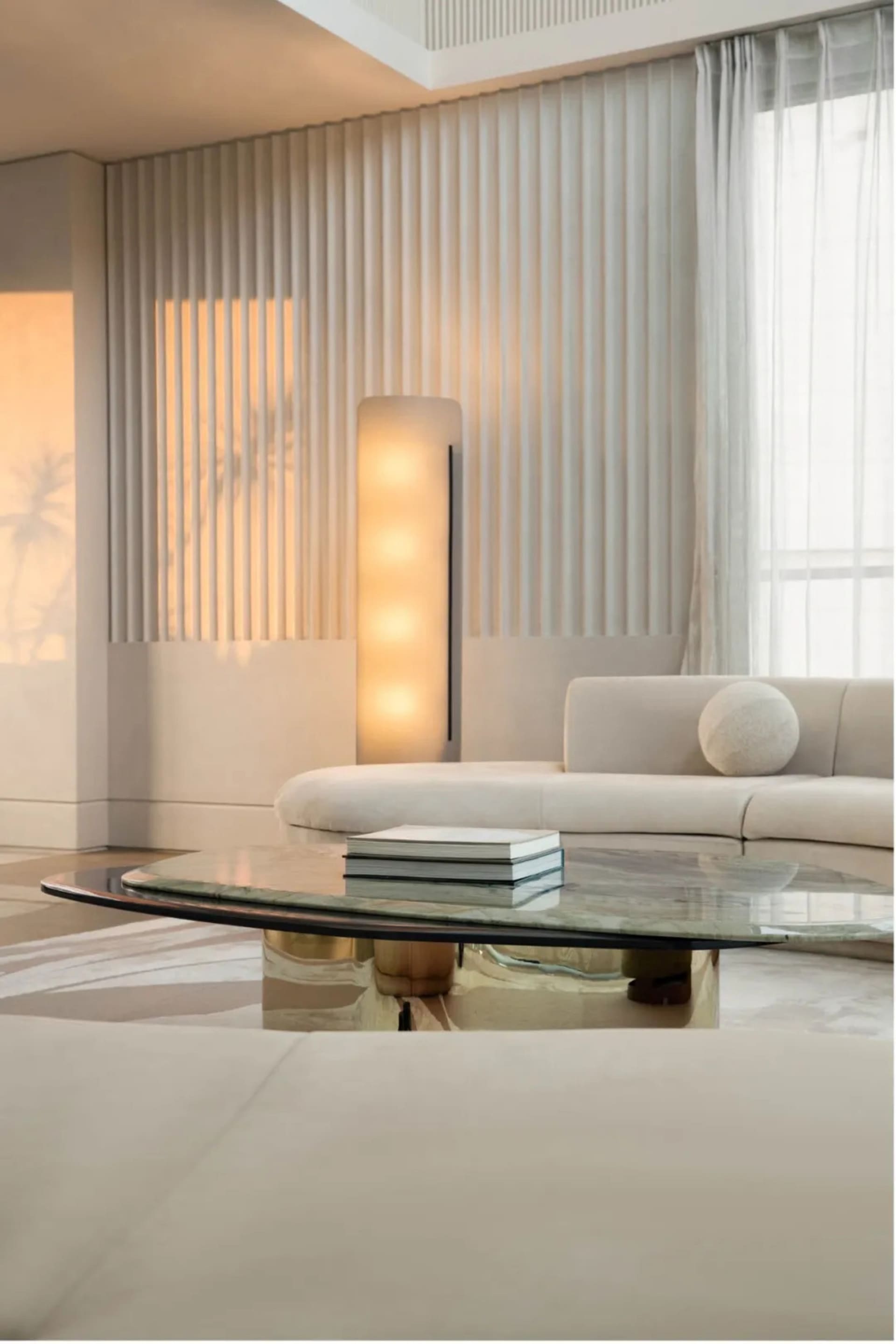 A minimalist living room featuring a white sofa, a glass coffee table, and a fabric curtain with vertical slats