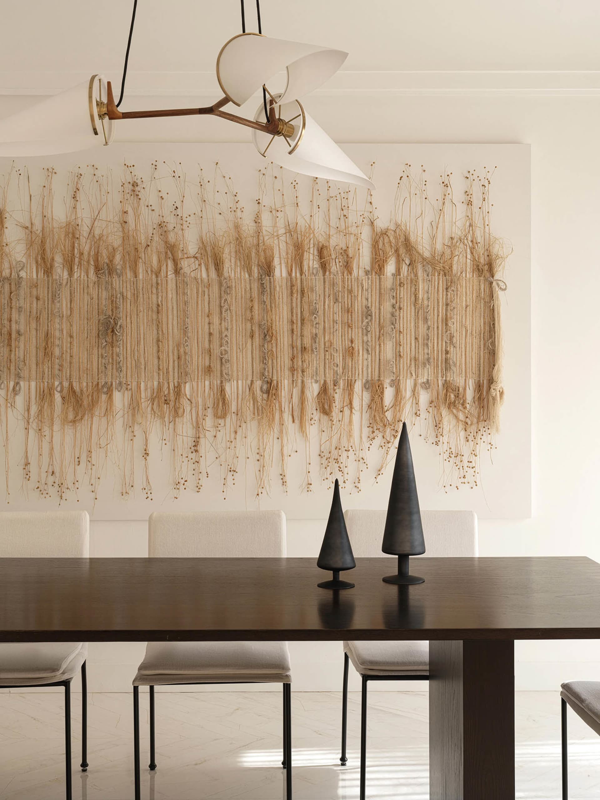 Modern dining room featuring a textured, hanging textile artwork on the wall, complemented by sleek dining table and chairs,