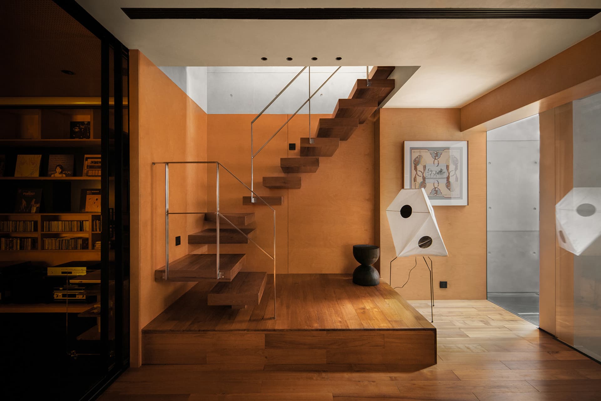 Modern residential interior with wooden stairs, glass railings, and metal accents.