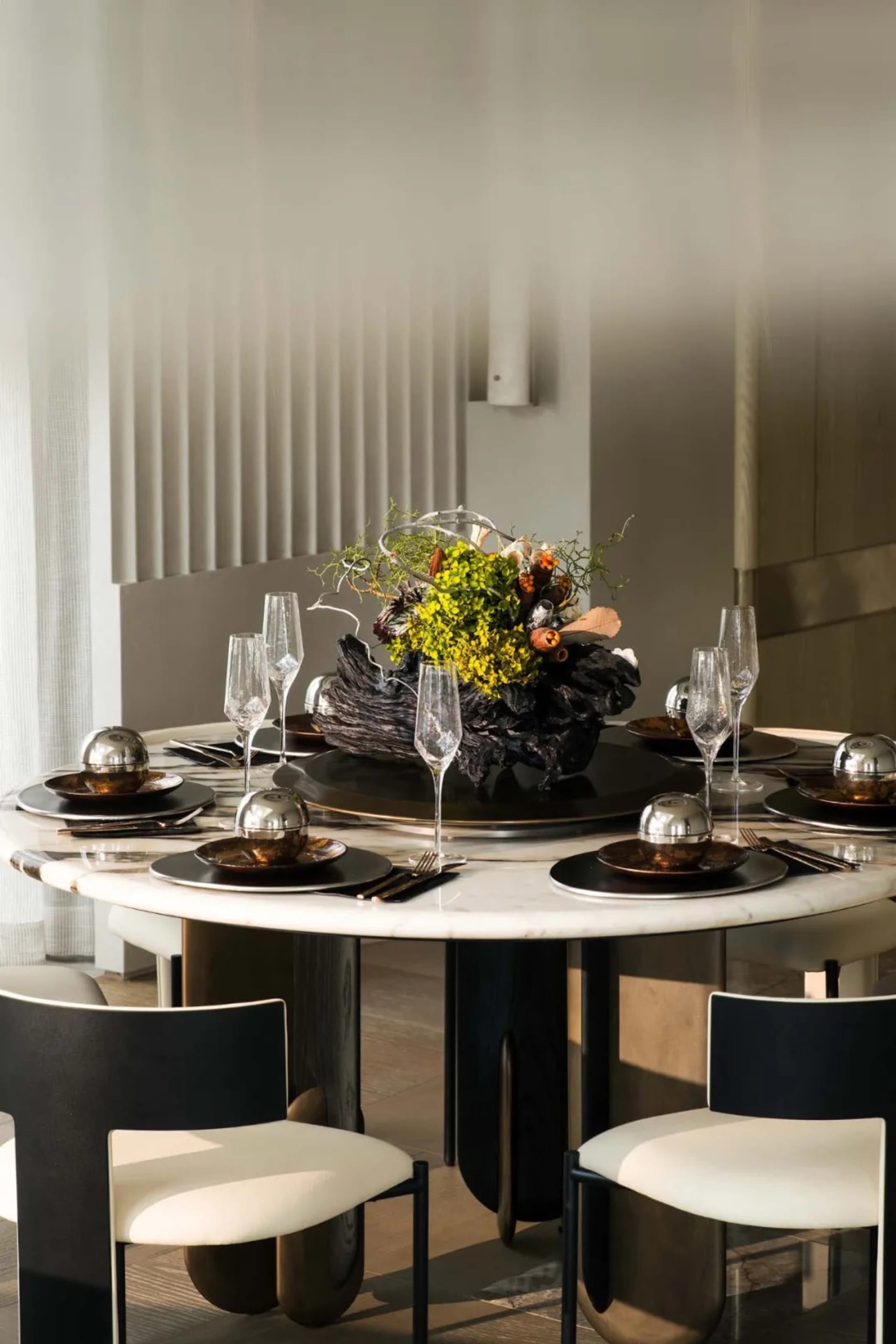 Modern dining table with marble top, surrounded by black and white chairs, featuring an artistic centerpiece with vibrant flo