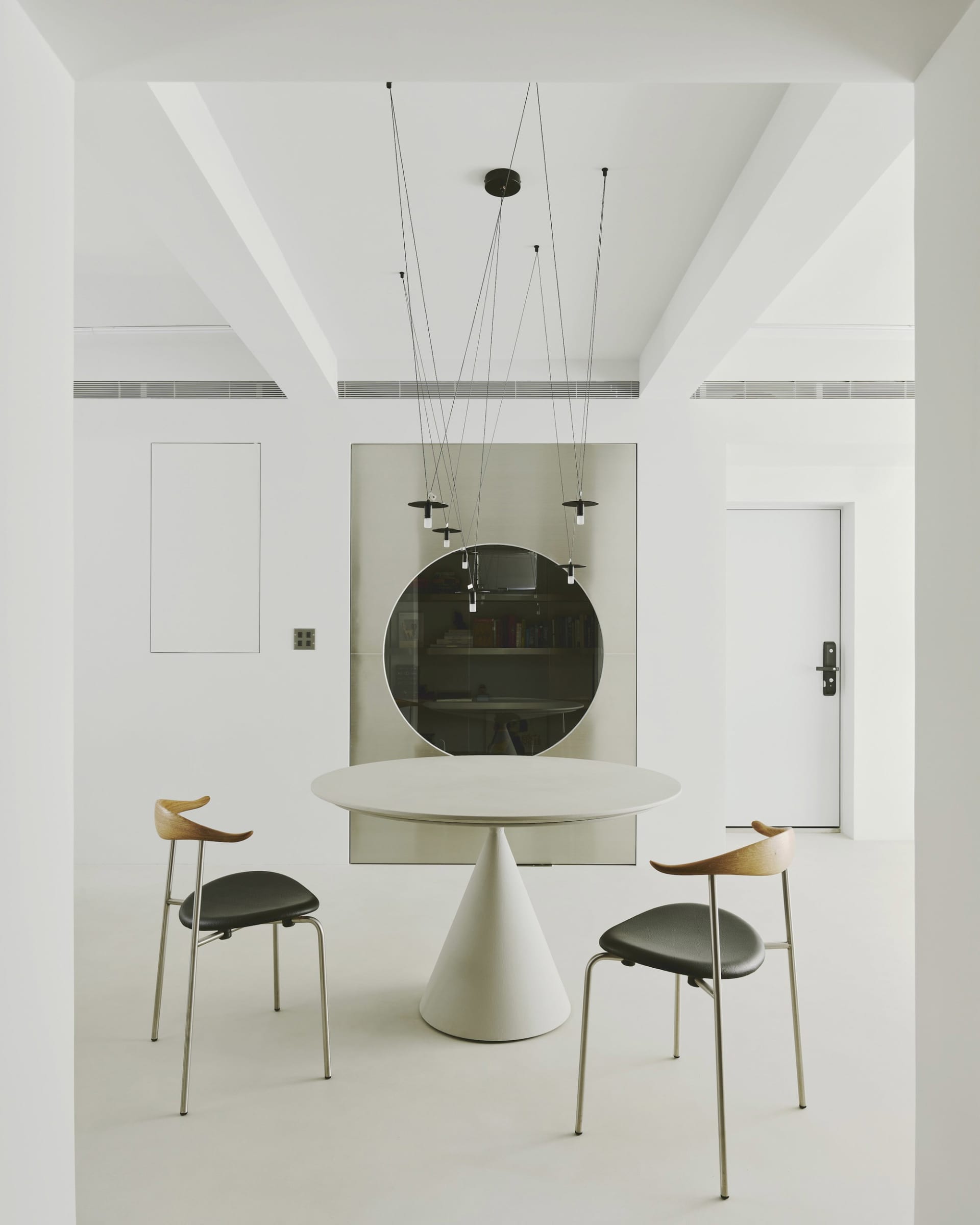 A modern dining room featuring a round table with a cone-shaped base and two chairs with black seats and wooden backs.