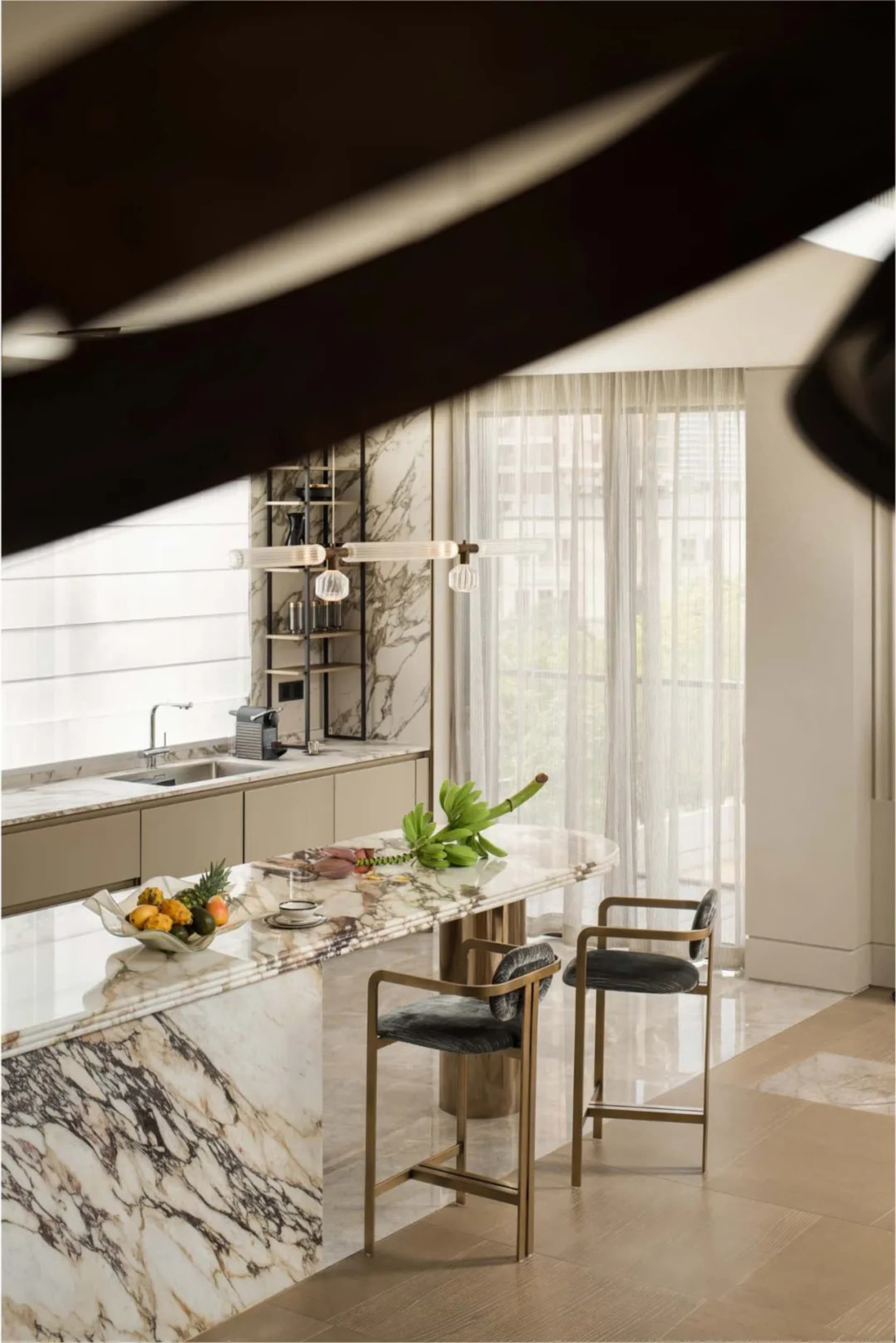 Modern kitchen featuring marble countertops and white chairs with a hanging light fixture and cityscape view.