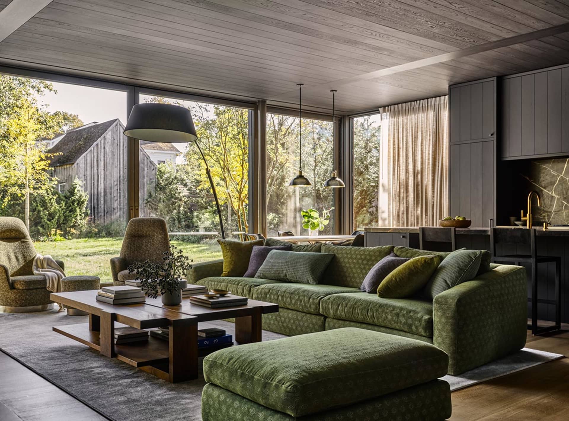Modern living room featuring a green sofa, wooden flooring, and large windows with a view of the garden.