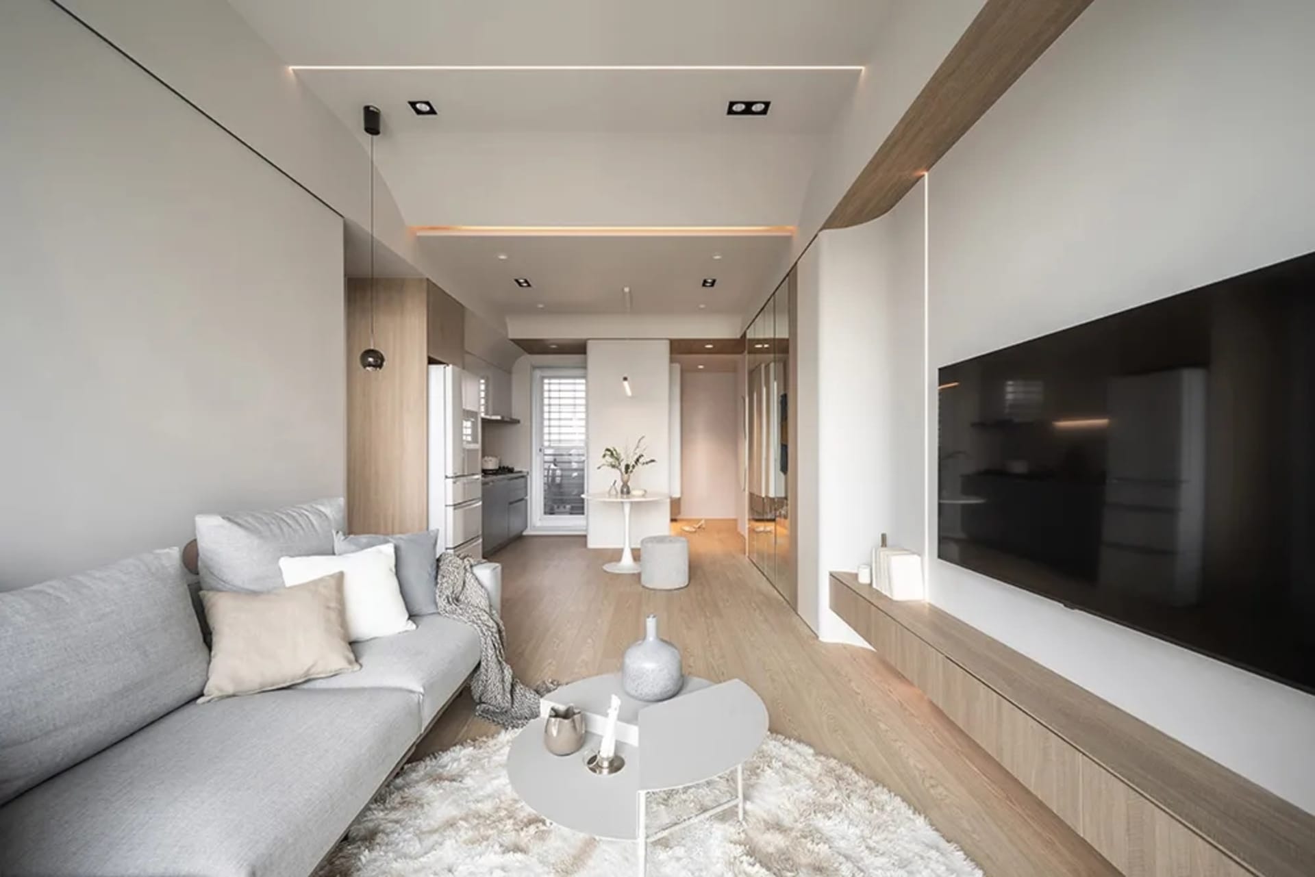 Modern living room featuring white walls, a grey sofa with white and beige throw pillows, and a wooden floor. A white coffee