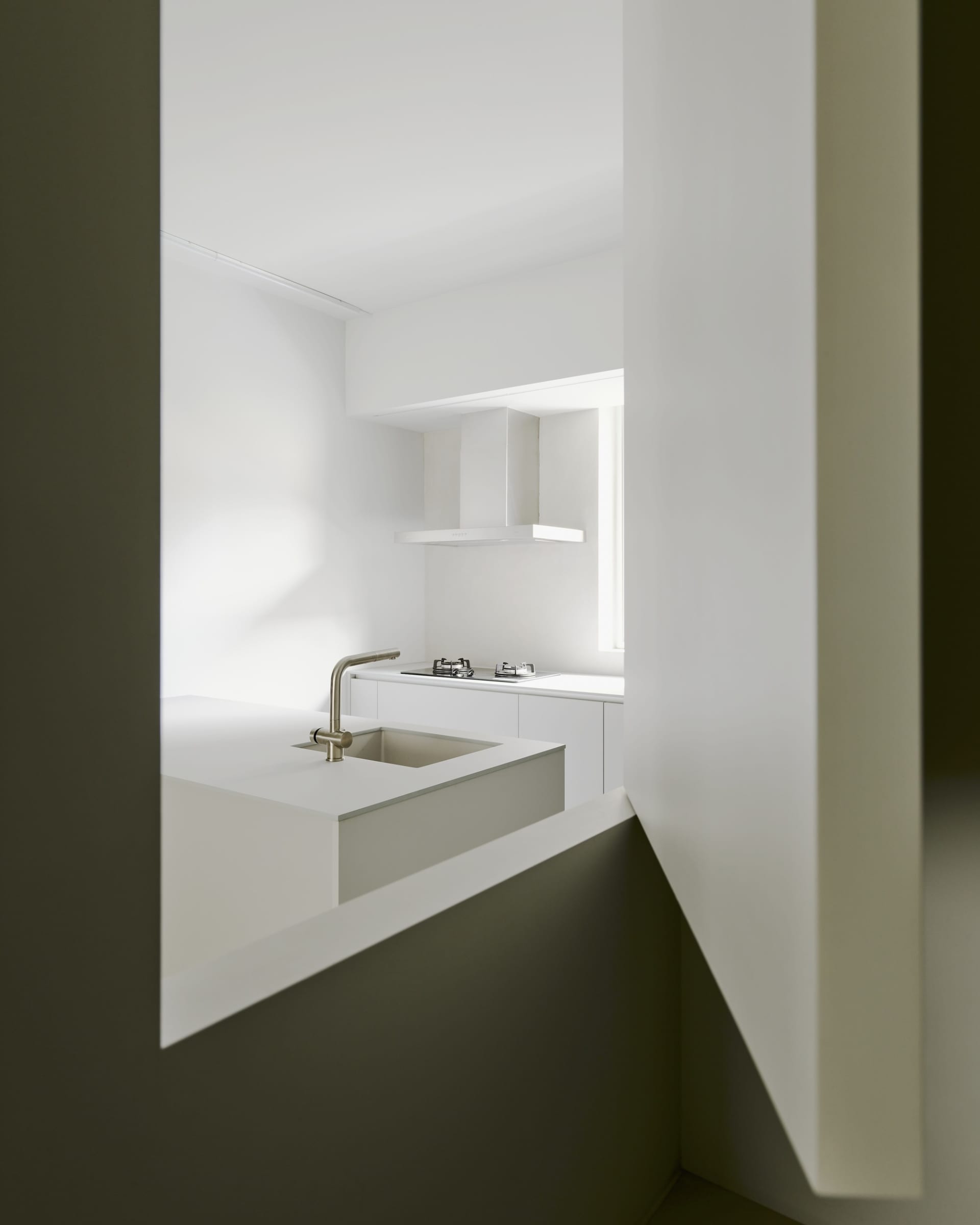 A modern kitchen with white countertops and walls, featuring a stainless steel faucet and a gas stove.