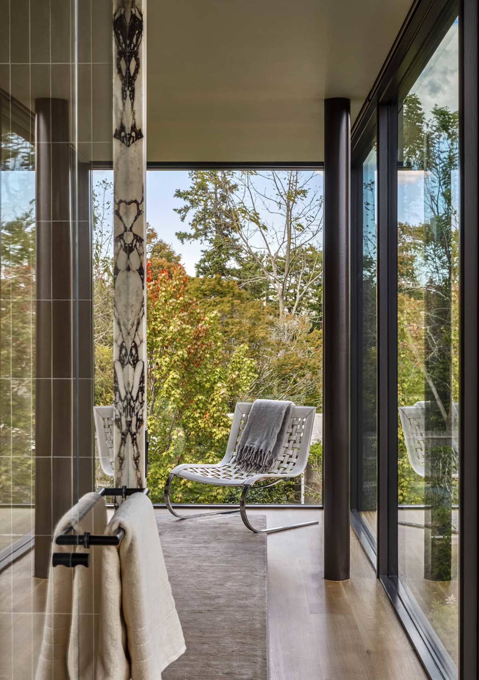 A modern minimalist living room with floor-to-ceiling windows, a white chair, and a towel rack.
