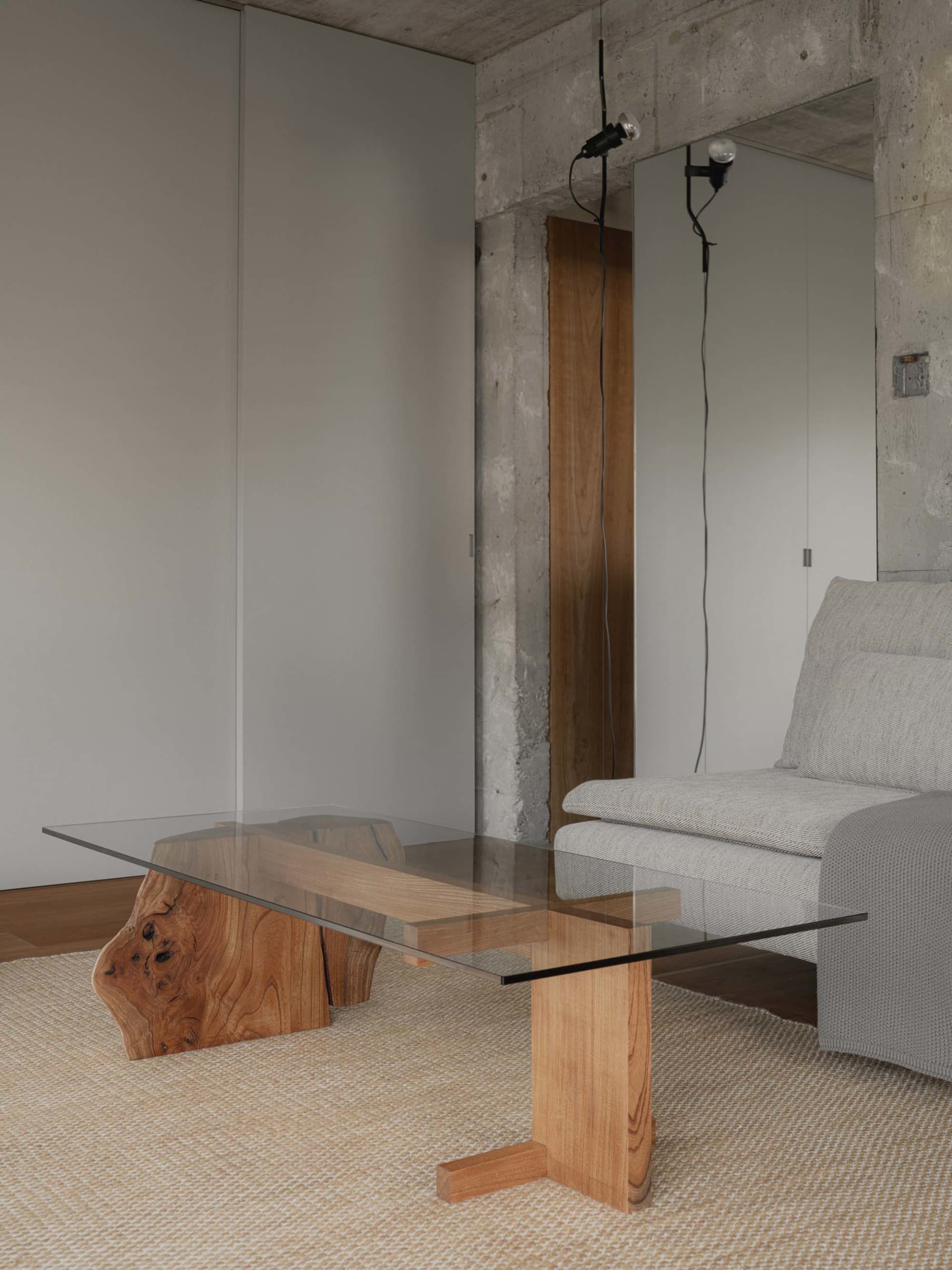Modern industrial interior living room with glass table, wooden elements, and concrete walls.