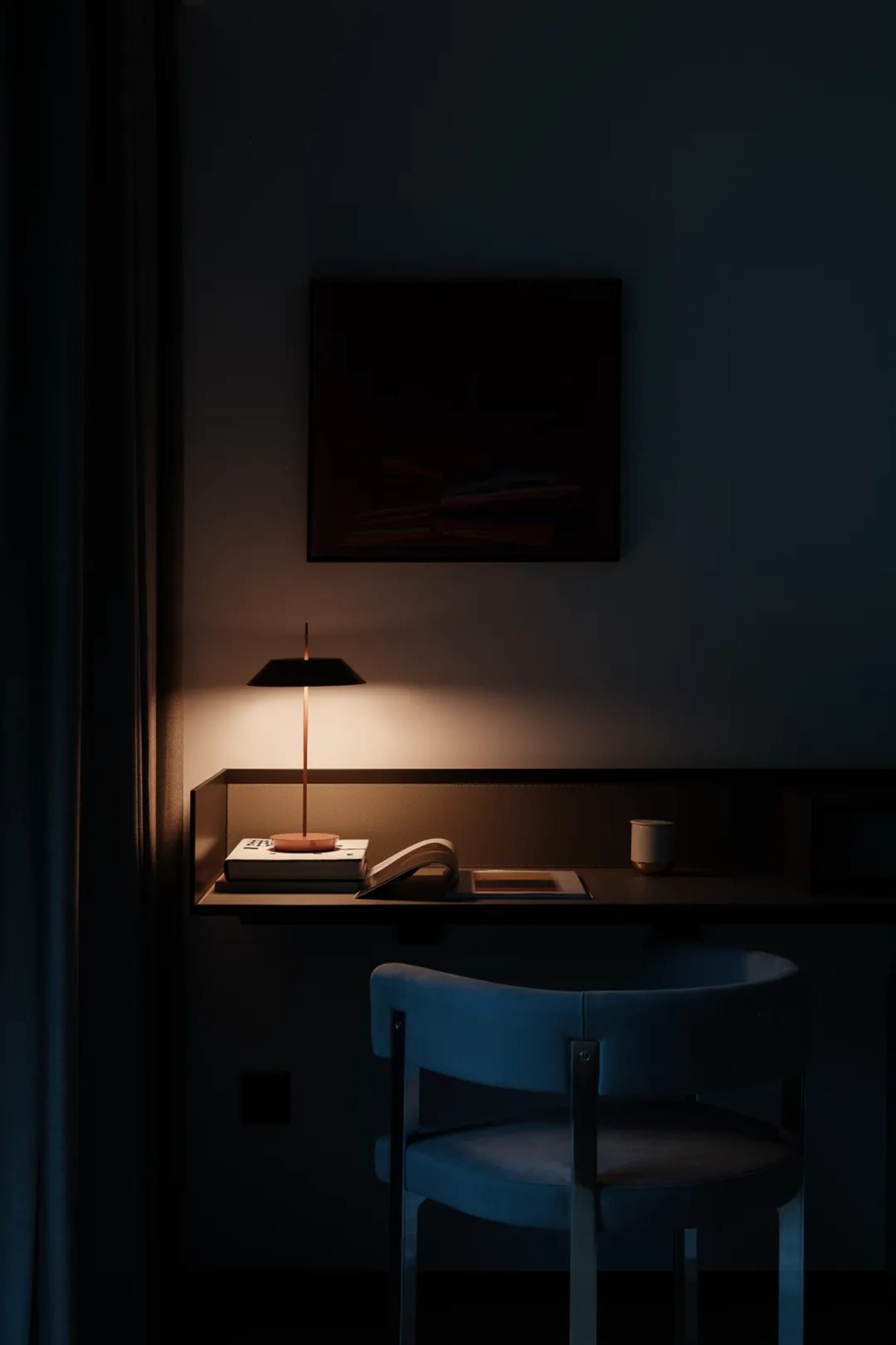 A minimalist desk with a wooden chair and lamp, featuring a black lampshade, books, and a cup.
