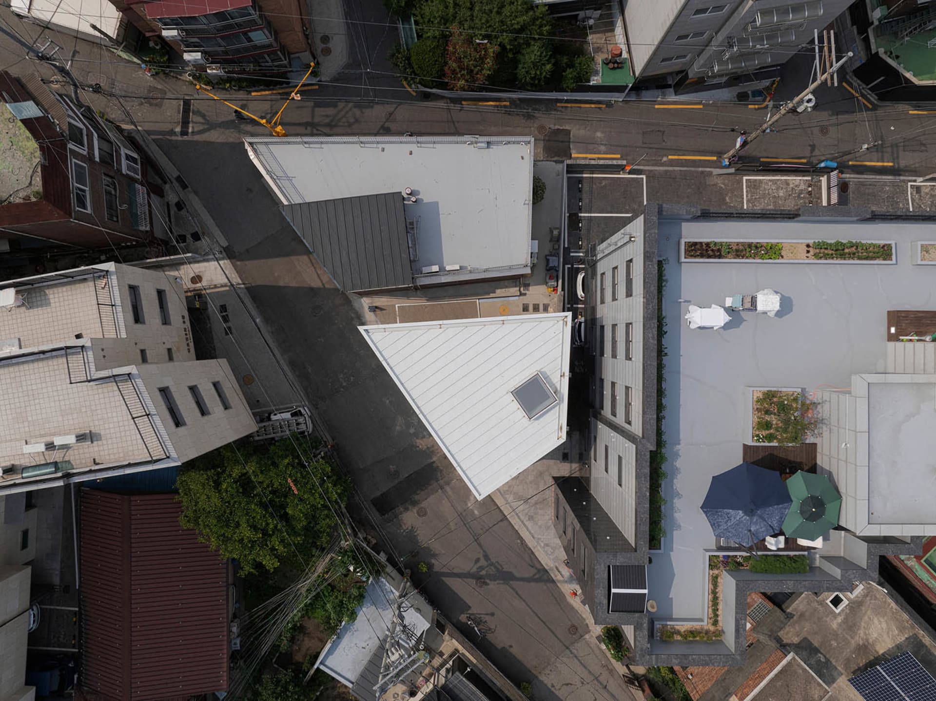Urban architecture with a rooftop garden featuring a white triangular structure and a green space with umbrellas.