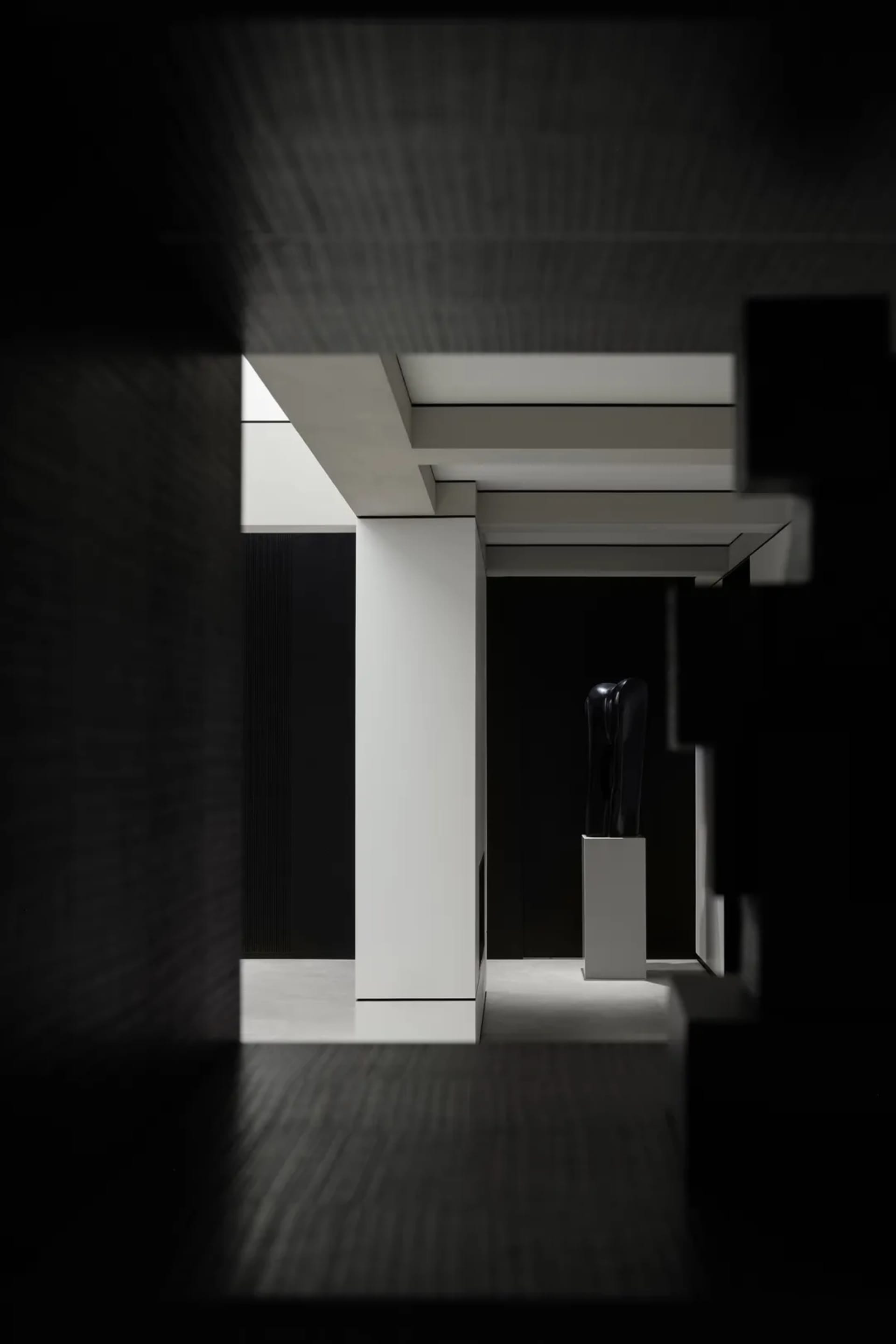 A minimalist interior with black and white elements, featuring concrete walls and a black sculpture.