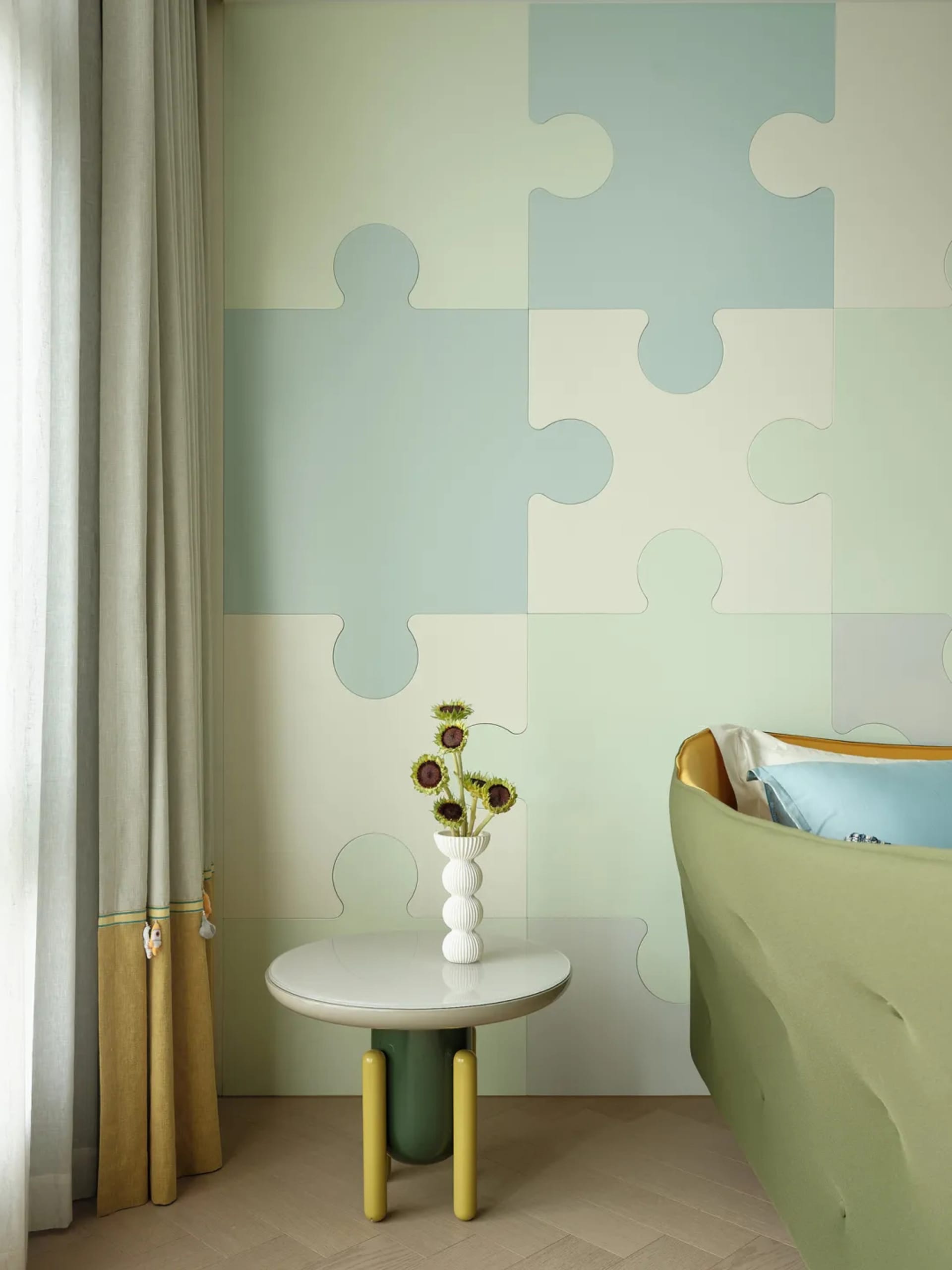 A bedroom featuring a wall covered with fabric panels, a green round table with a vase of sunflowers, and a blue and yellow b