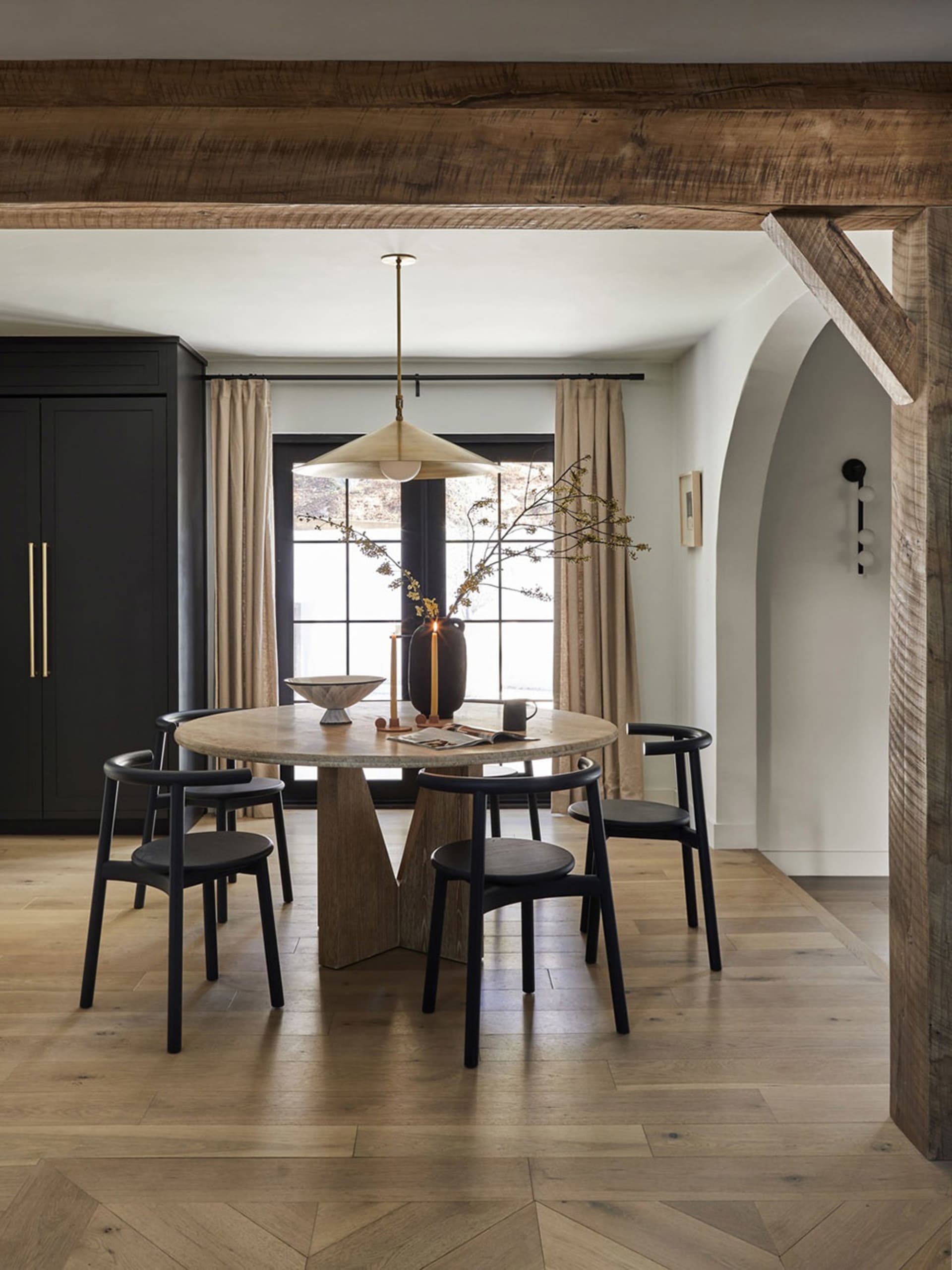 A modern dining room featuring wooden beams, a round table, and black chairs.