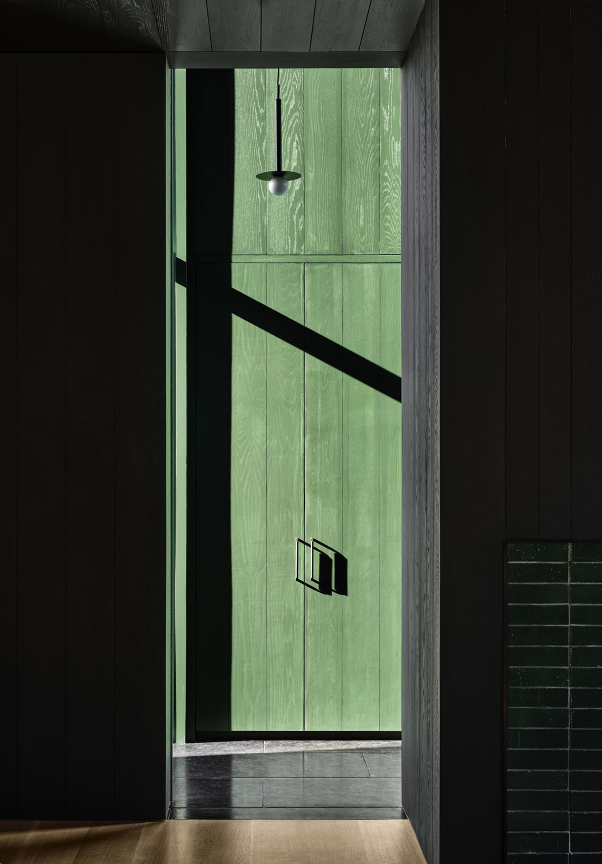 A modern green wooden doorway with sunlight casting a shadow