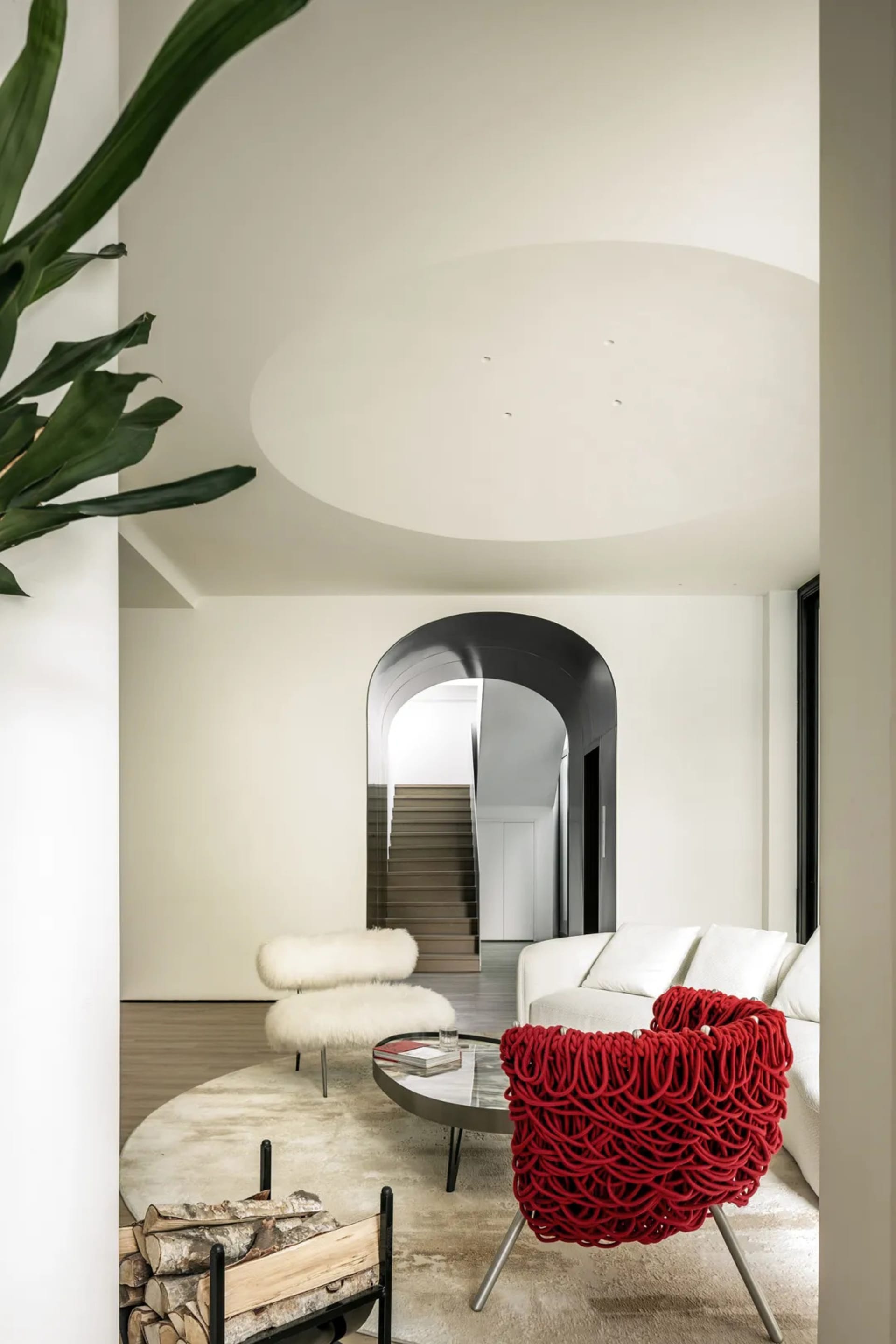 Modern, minimalist living room featuring a white sofa, red armchair, and white furry ottoman.