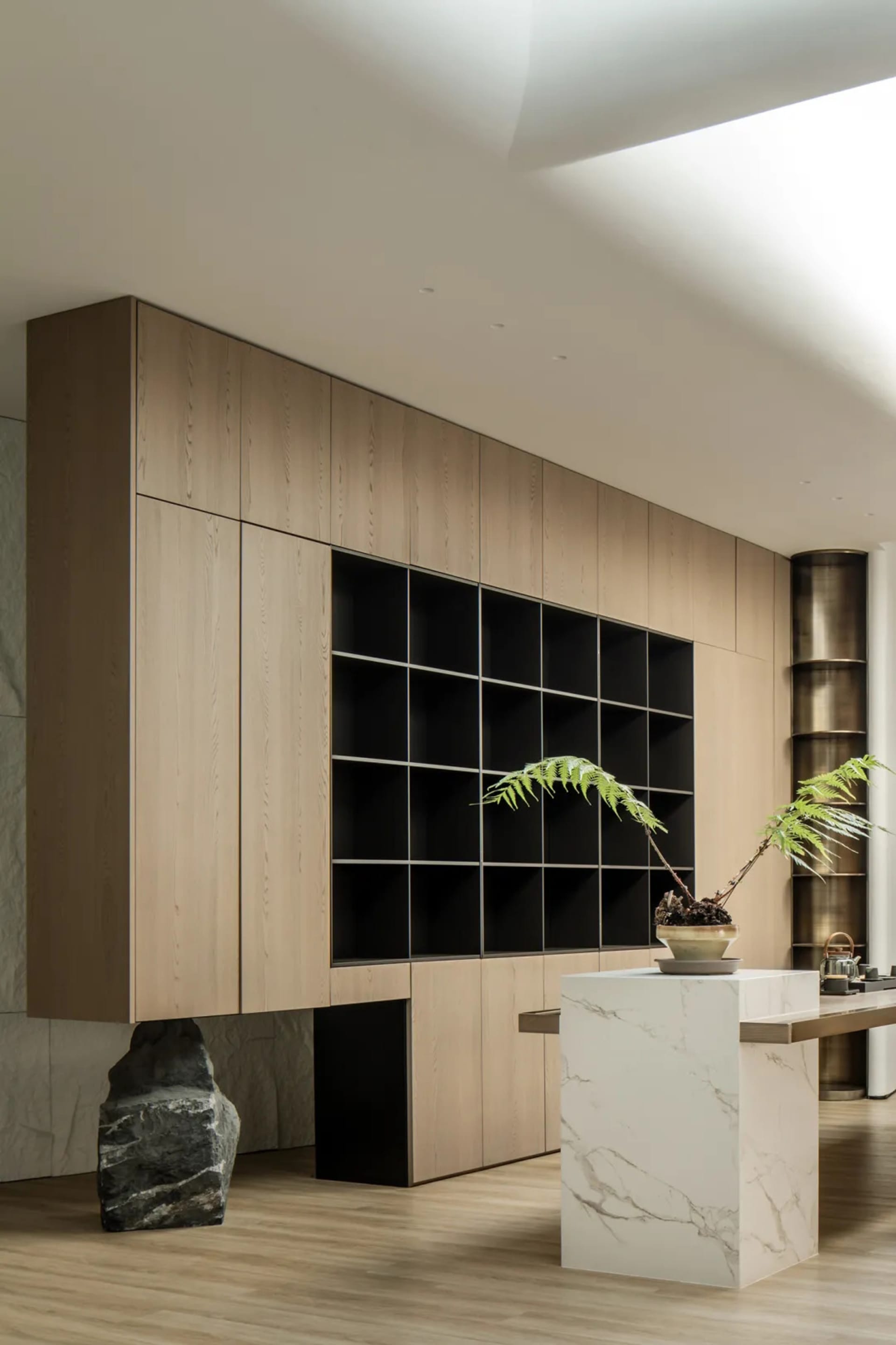 A modern living room and library featuring wooden shelving, leather seating, marble tables, metal accents, and potted plants.