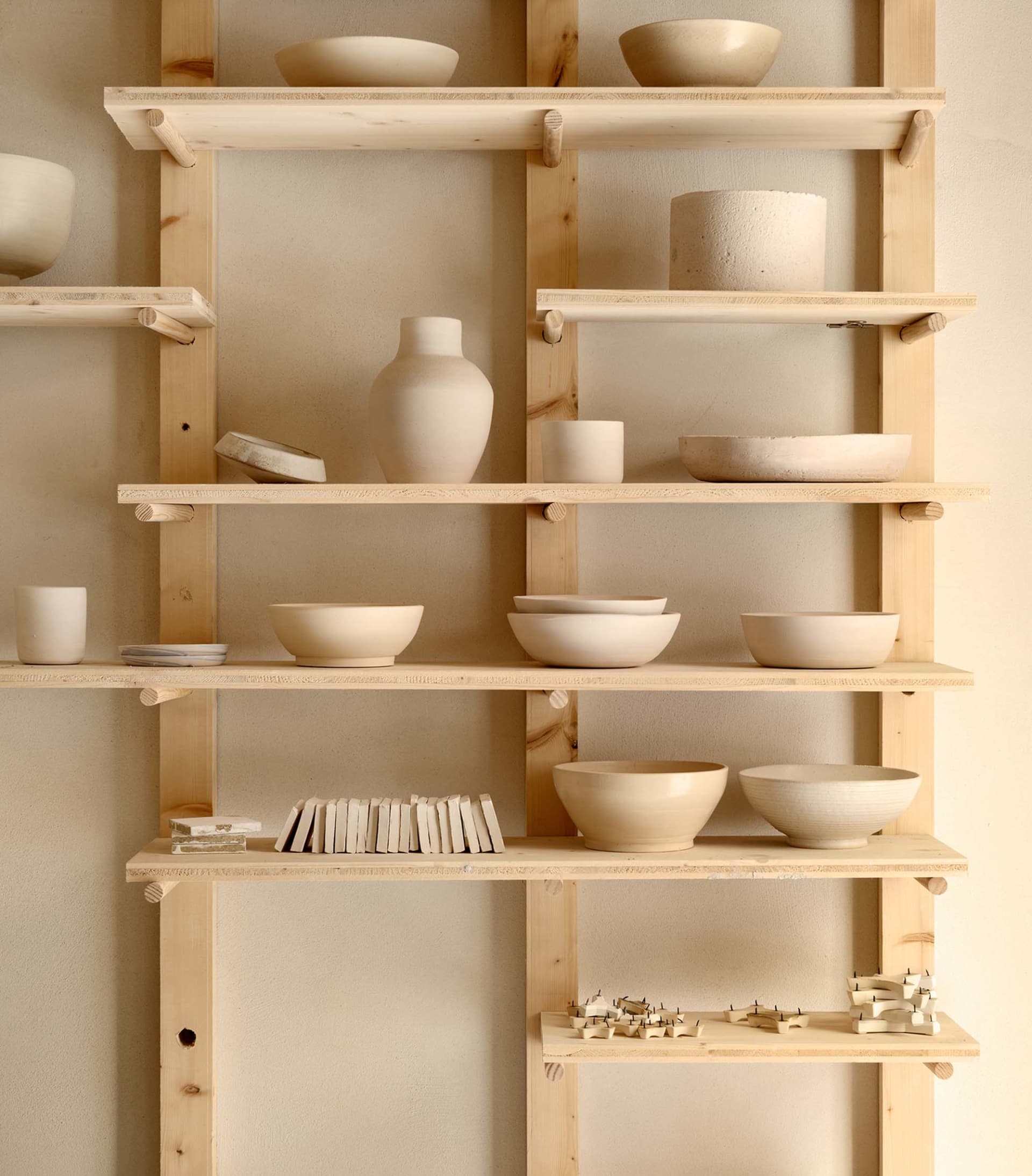 A minimalistic display of ceramic bowls and vases on wooden shelves.