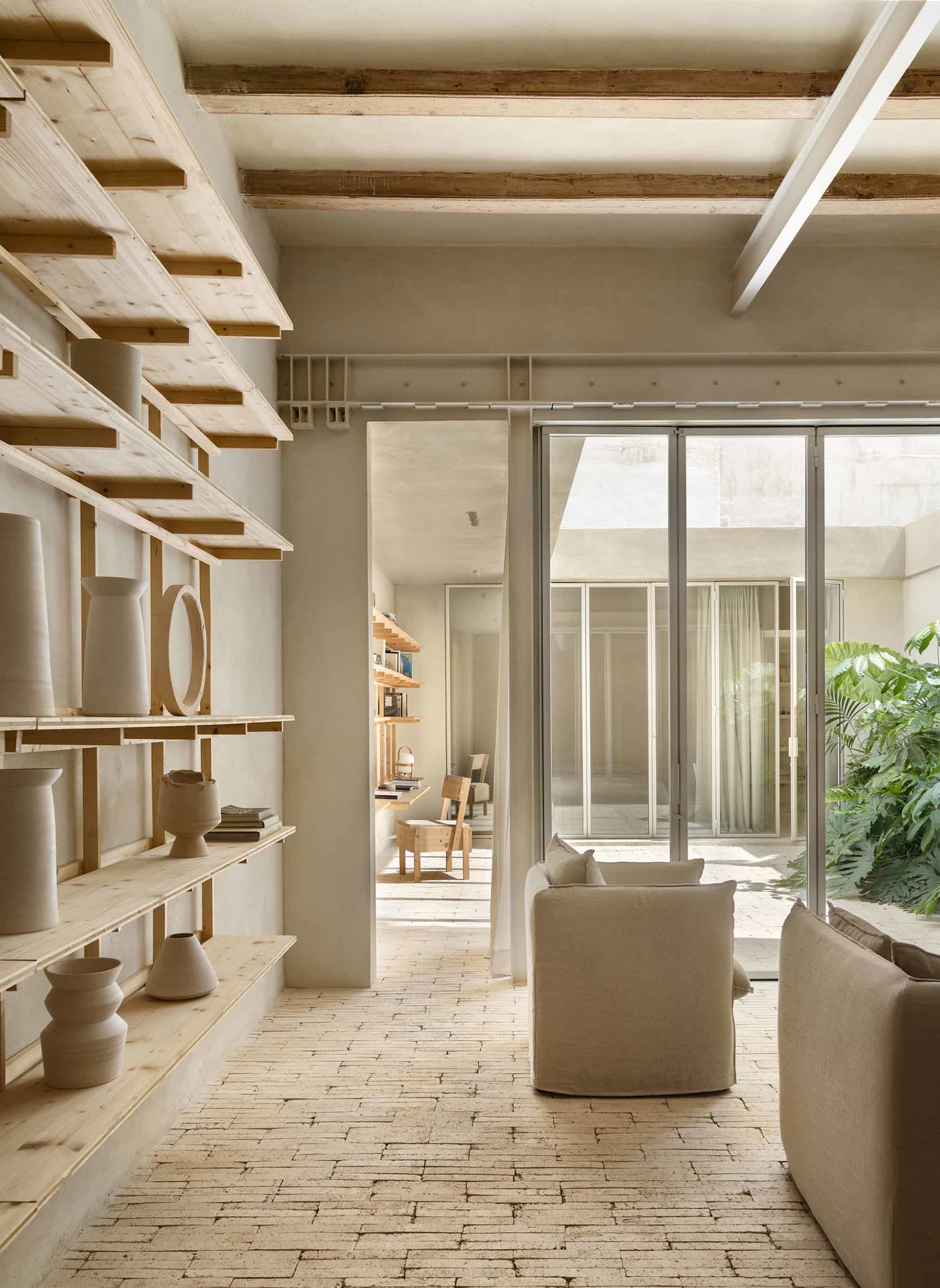 A minimalist living room with concrete walls, wooden furniture, and glass partitions.
