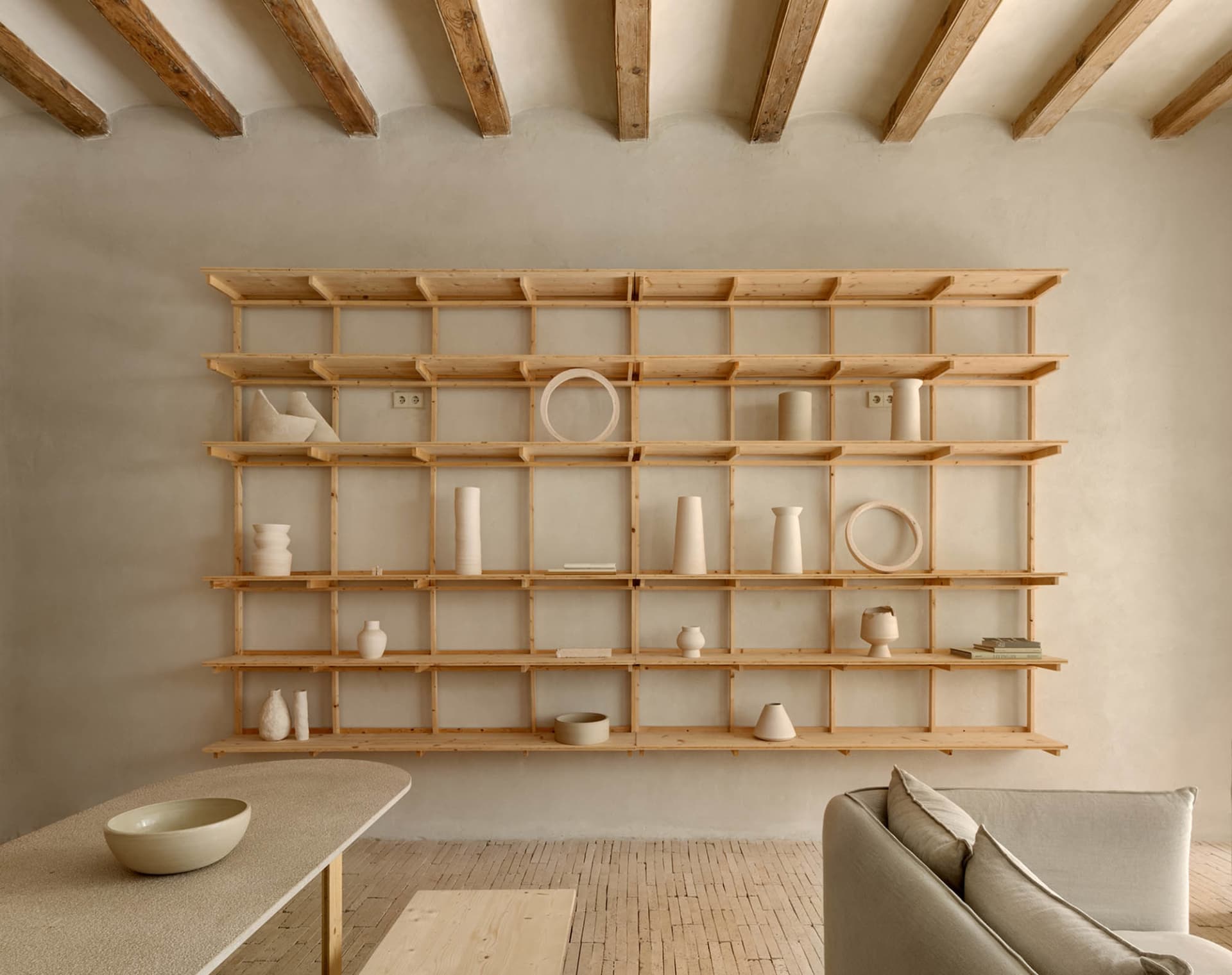 A minimalist shelf display featuring various wooden objects in a serene, neutral-toned room.