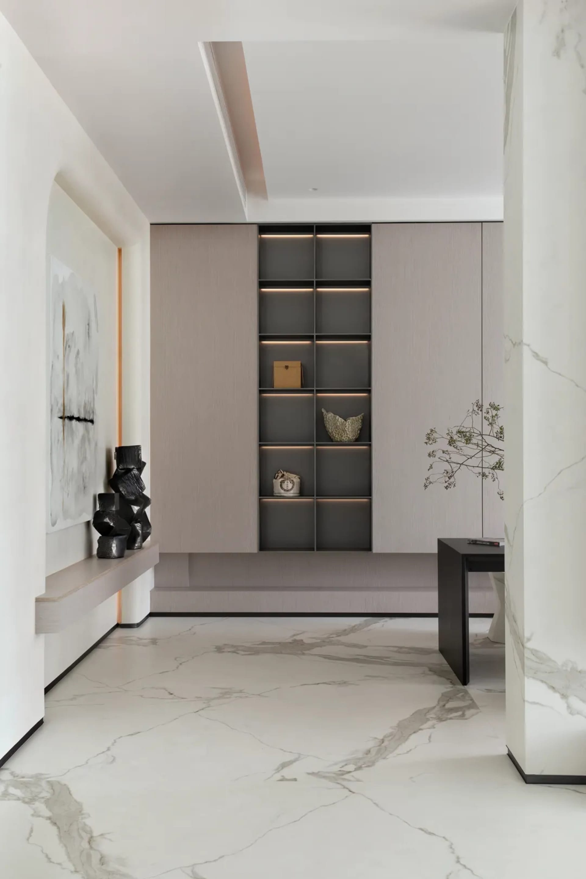Modern entrance hall designed with marble flooring and walls, featuring a minimalist bookshelf and a contemporary table.