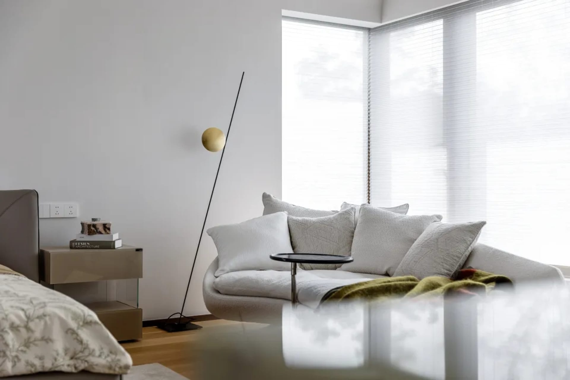 A modern living room featuring a light wood floor and upholstered furniture, with a minimalist lamp and a white sofa adorned