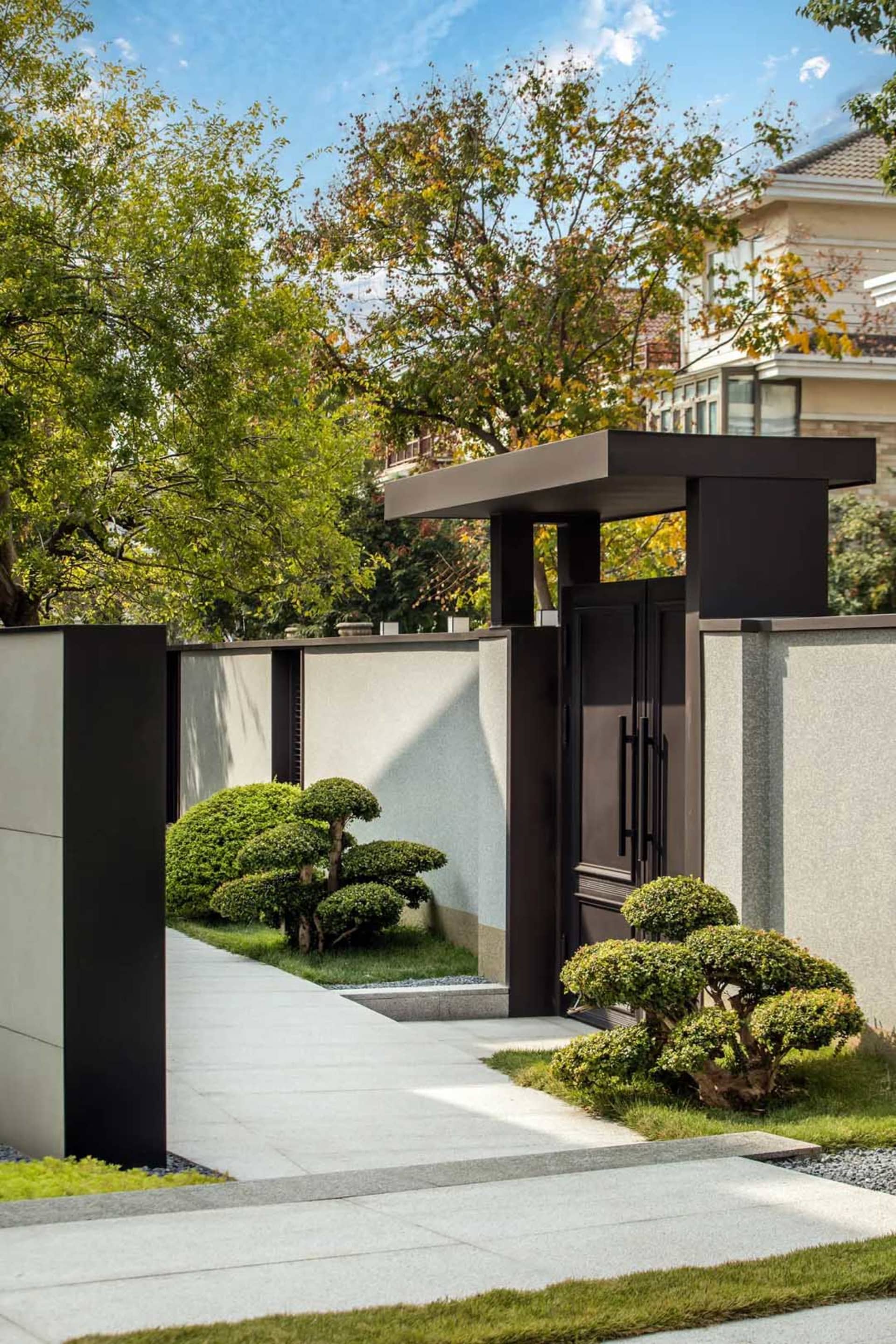 Concrete and metal entrance with small bonsai trees and greenery surrounding it.