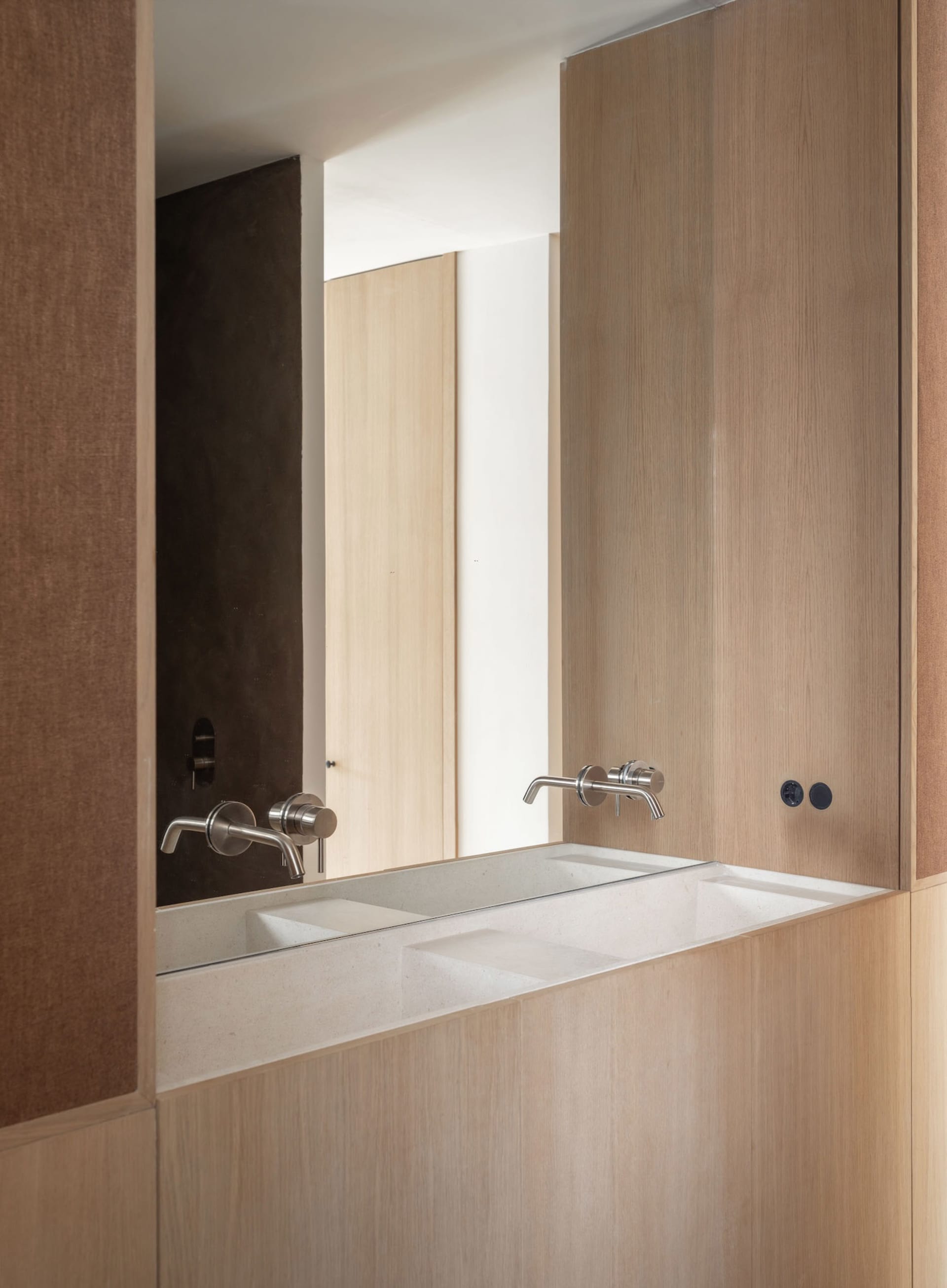 Modern minimalist bathroom with wooden fixtures and a long, rectangular sink with faucets.